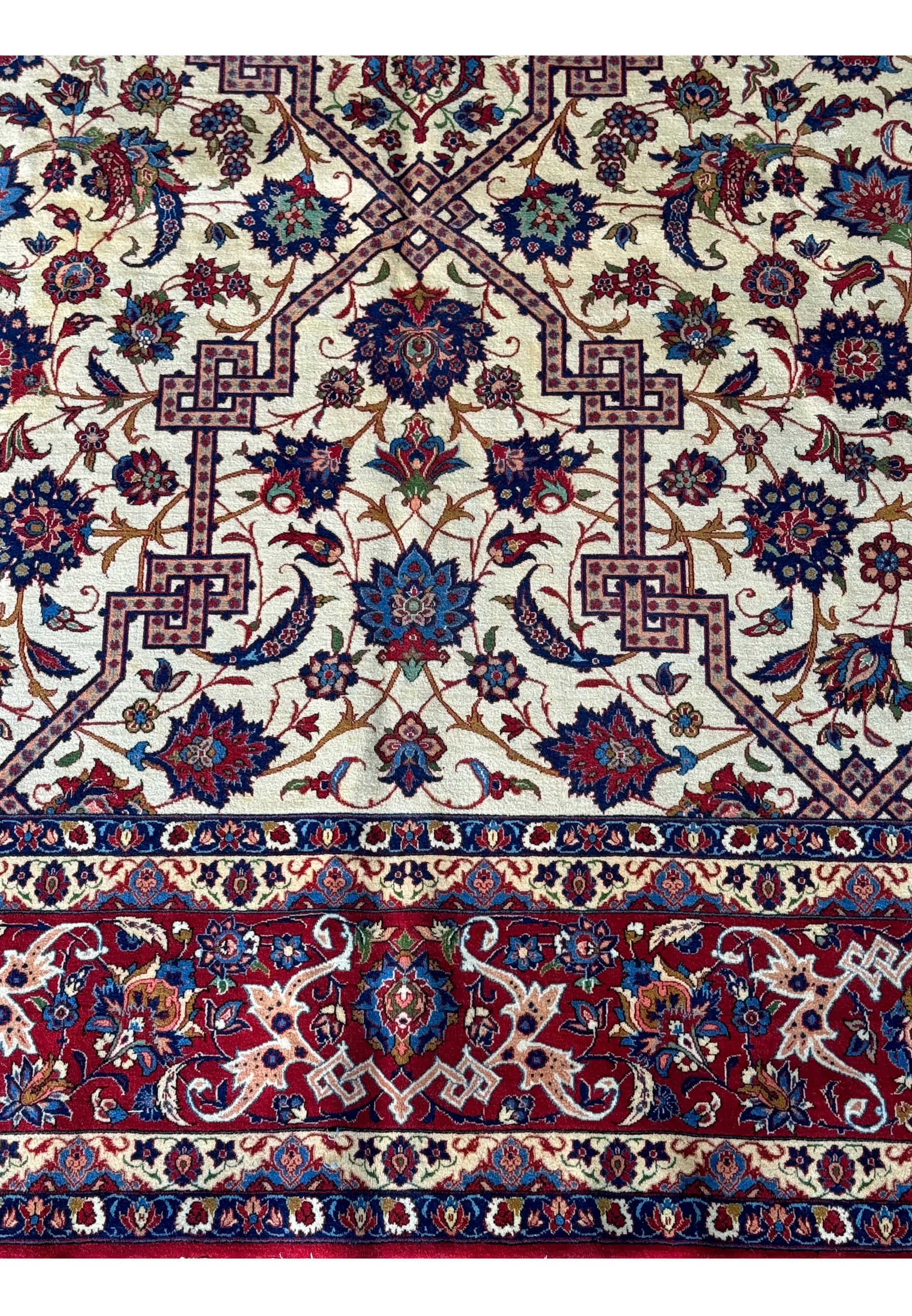 ull view of the Persian Isfahan rug on a flat surface highlighting the detailed overall pattern with a creamy ivory background and red borders.