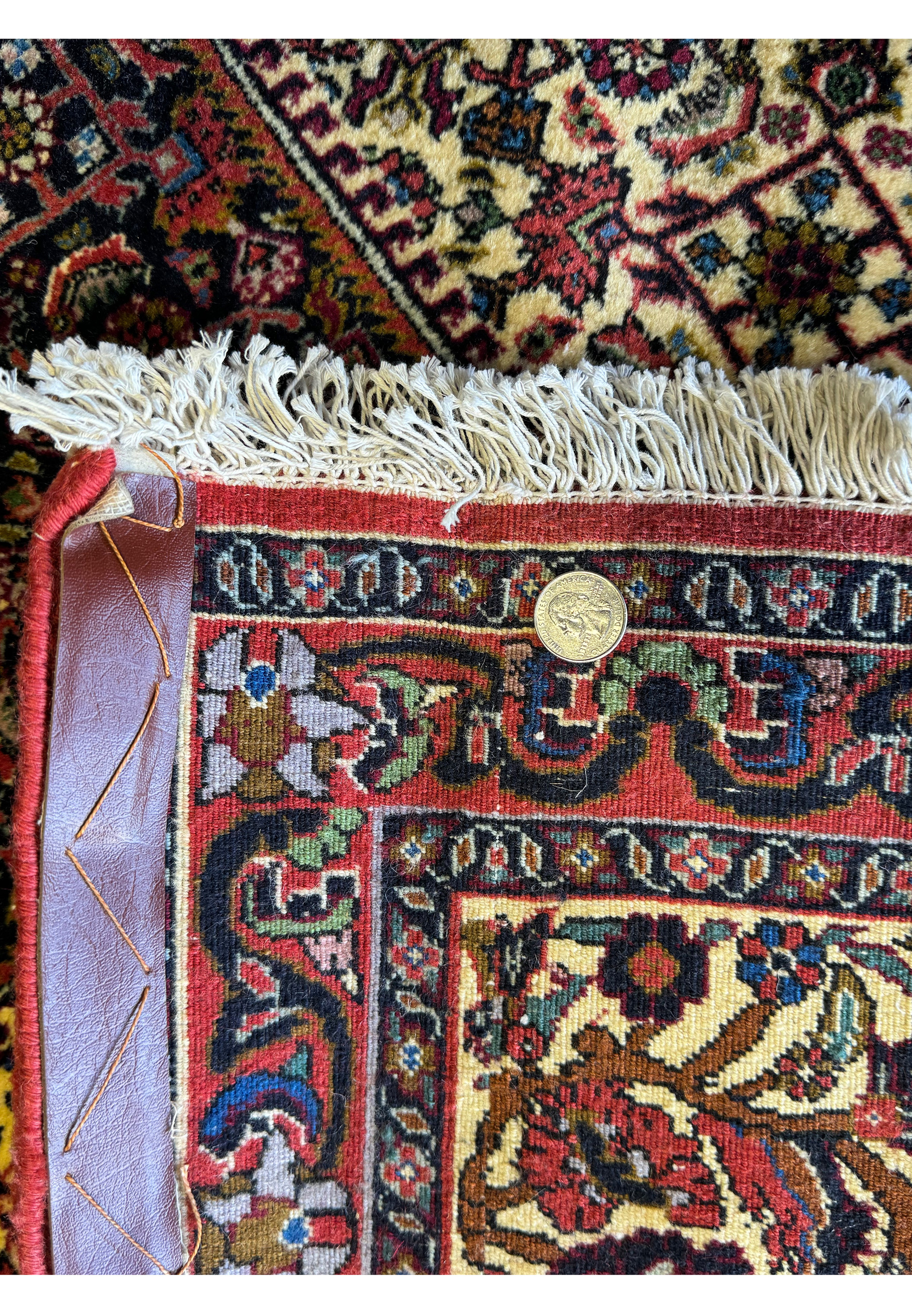 A close-up view of the Bijar rug's corner, where the quarter sits on the detailed backside border, offering a sense of scale to the dense patterns and the fine texture of the rug’s weave