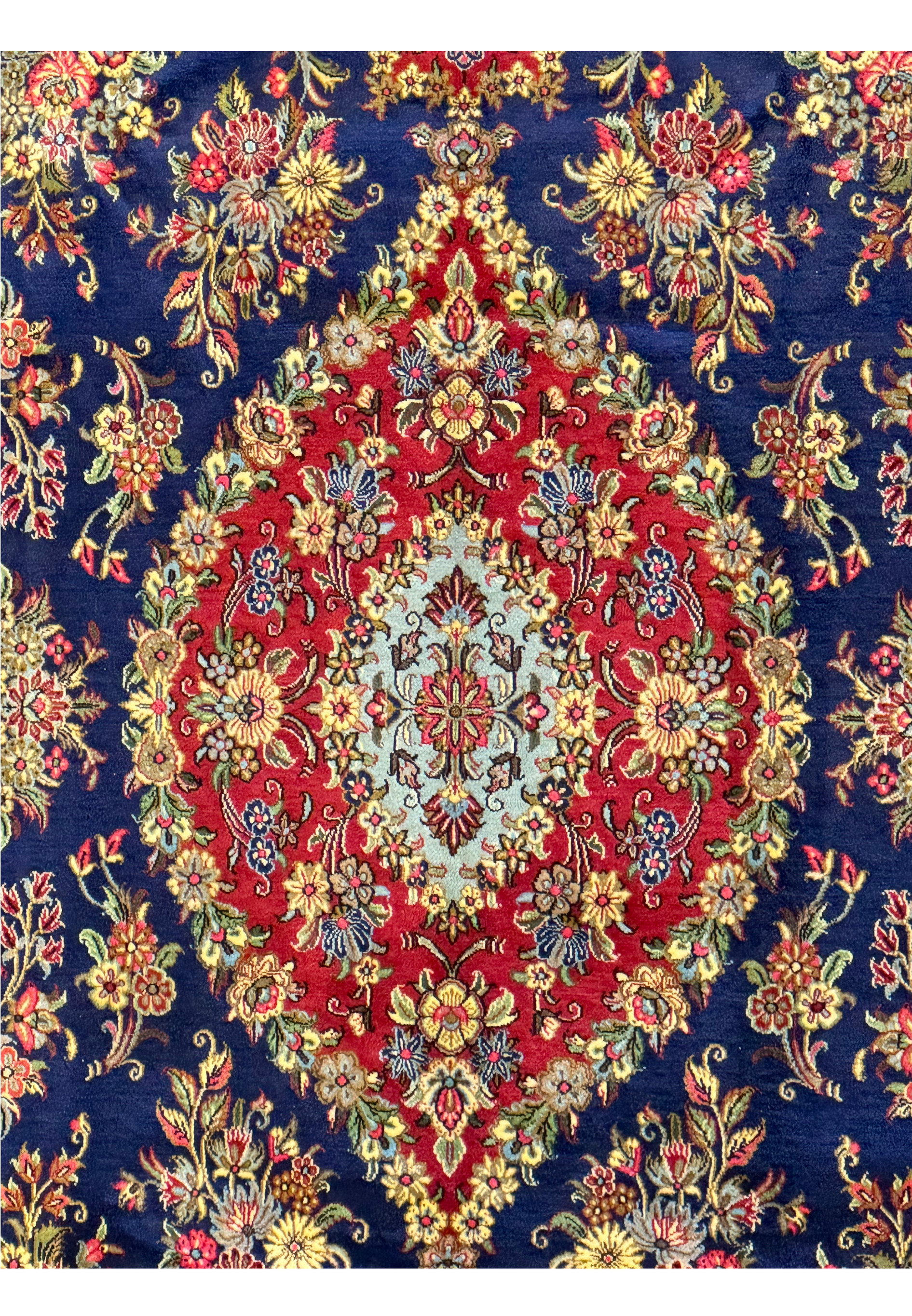 Close-up view of the central medallion on a Persian Qum Kork rug, detailed in red and cream with a complex array of floral designs and ornate patterns against a navy blue background