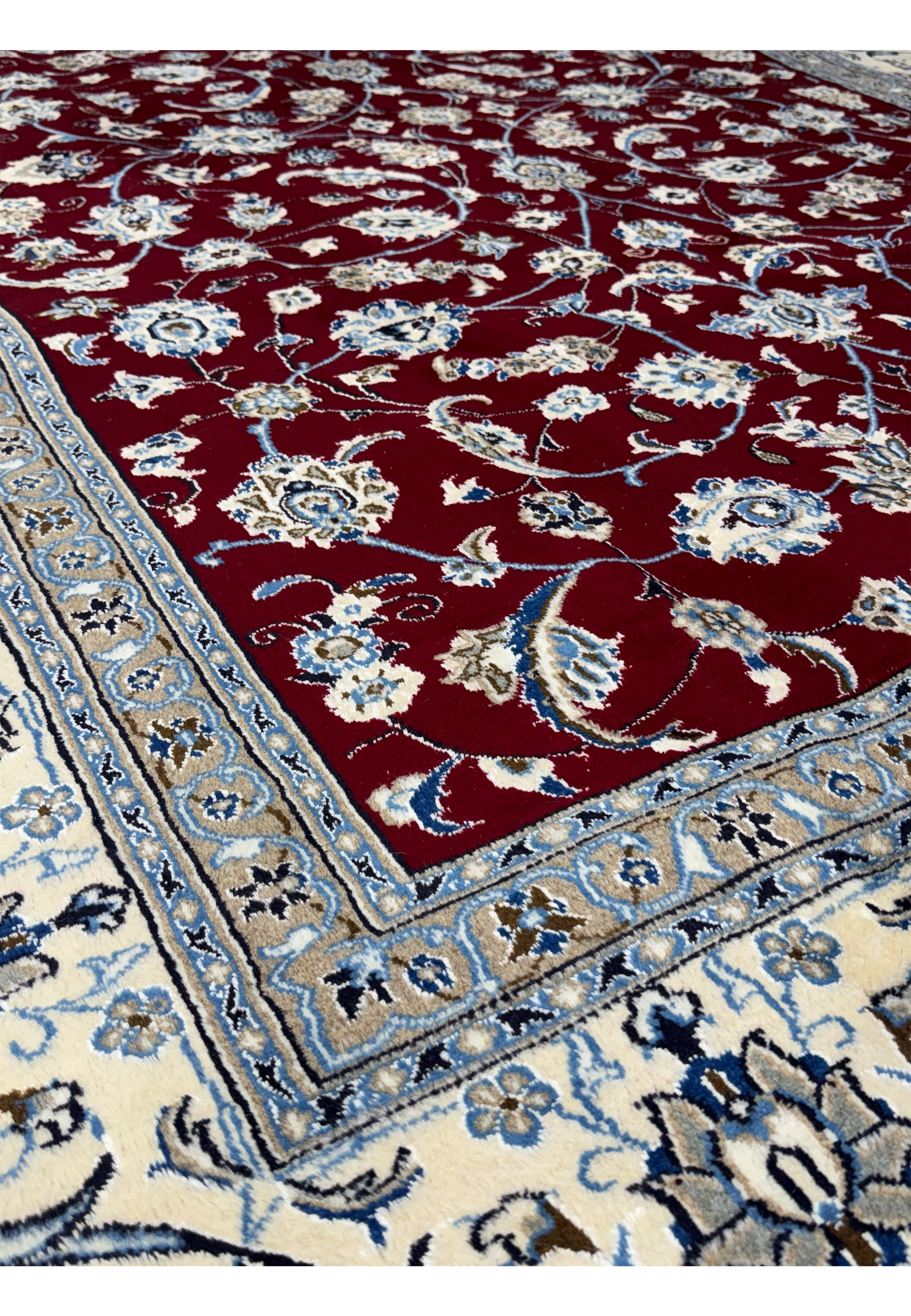 Close-up on the intricate border patterns of the Persian Nain 9La rug, featuring sophisticated floral motifs in navy and cream on a light blue background.