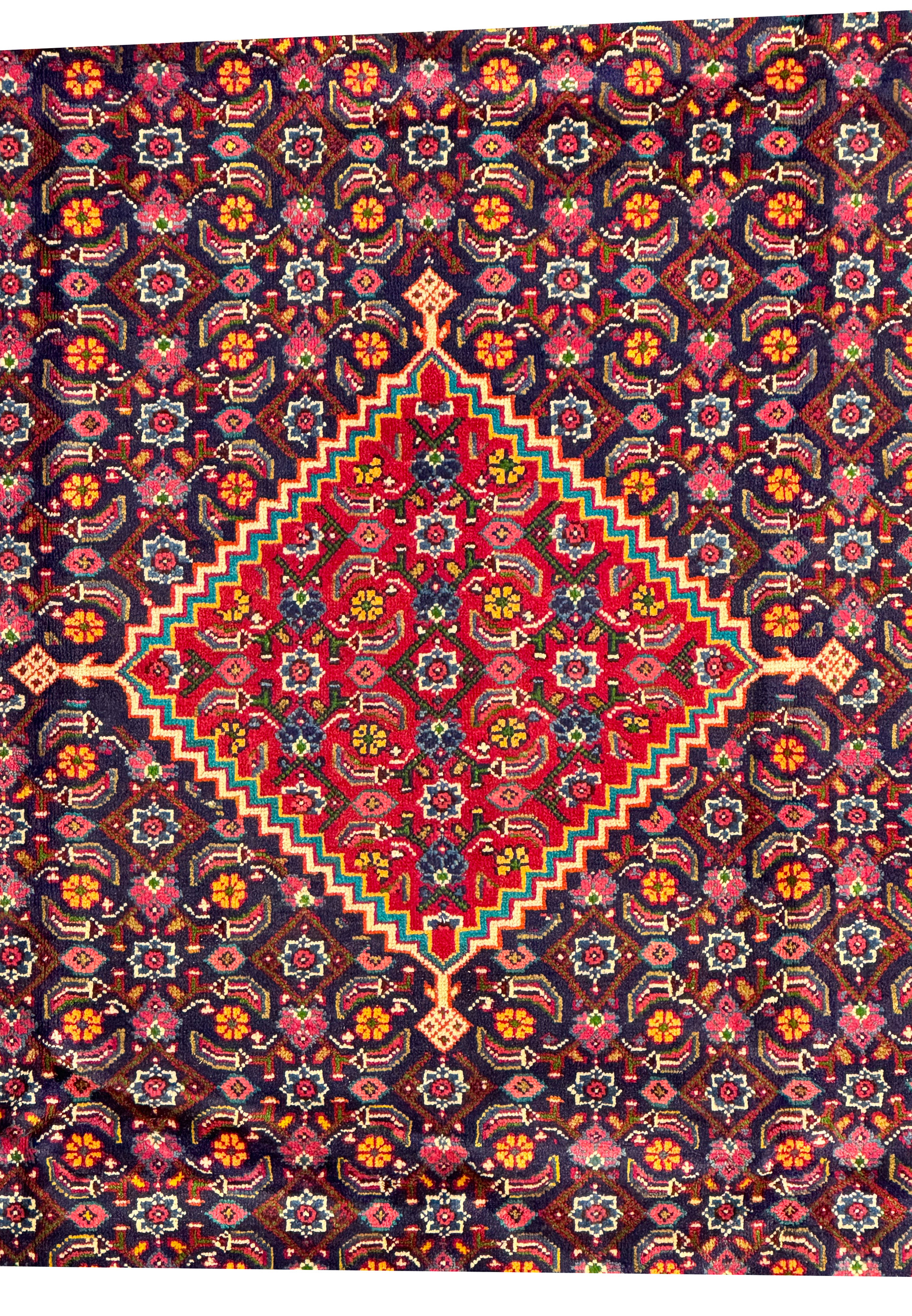 Close-up of the central medallion of a Persian Mahal Rug, featuring complex floral designs in a vibrant red and navy background. The detailed craftsmanship of the hand-knotted wool is evident in the intricate patterns and vibrant colors. This close-up allows for an appreciation of the fine details and the harmonious use of color that is characteristic of high-quality Mahal rugs, making it a focal point in any space
