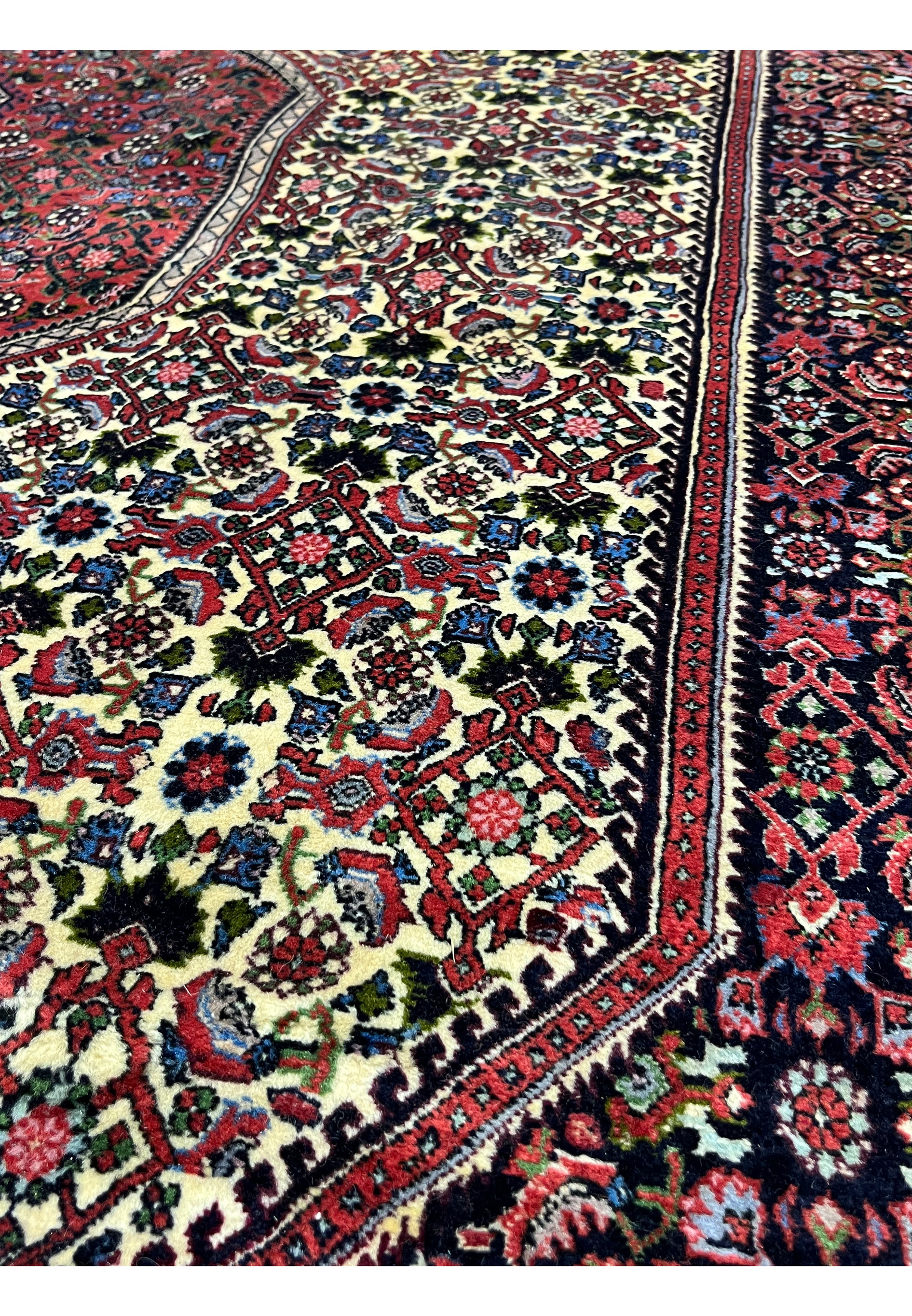 Pattern close-up of a Persian Bijar rug revealing dense knot structure, repeating Kurdish motifs, saturated reds, blues, and ivory tones with sharp definition.