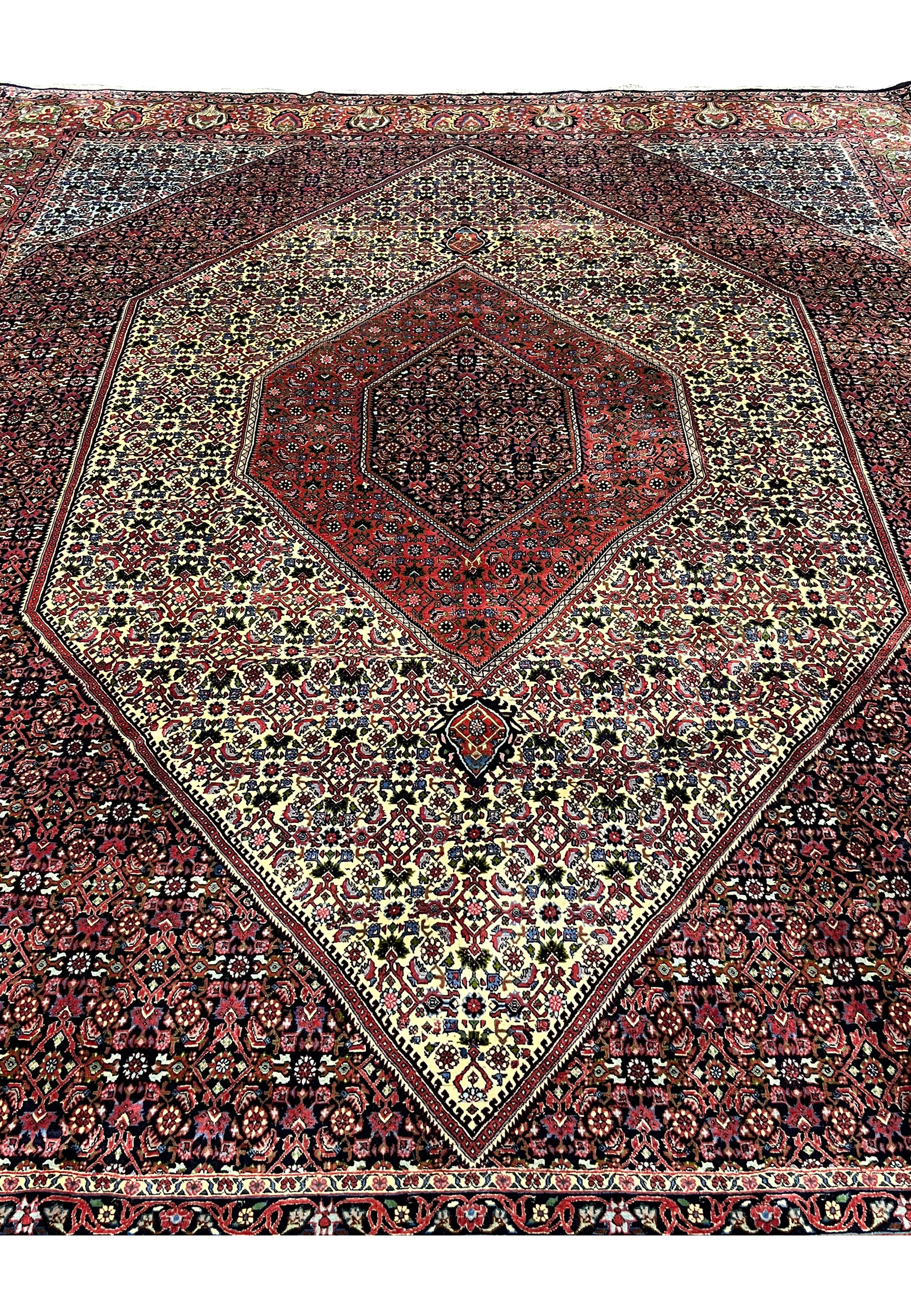Angled perspective of a 9.8 x 12.2 Persian Bijar rug showing dense hand-knotted wool, rich red tones, ivory field sections, and the rug’s heavy iron-weave construction.
