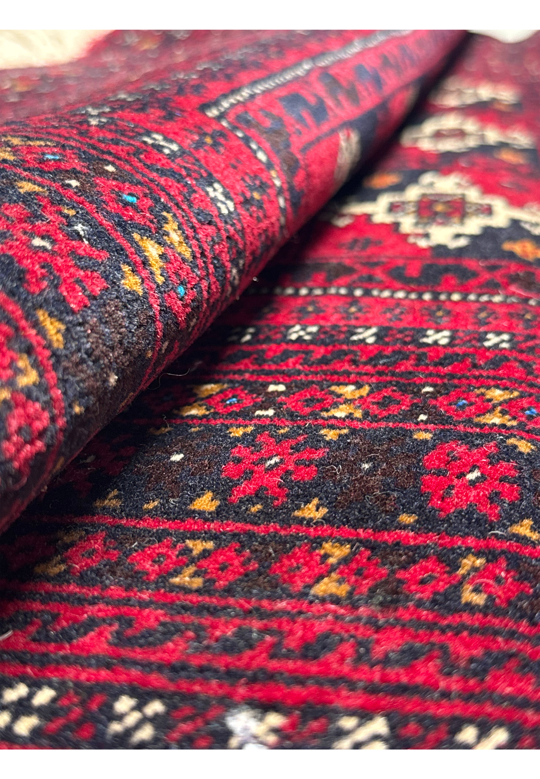 Rolled 3'6 x 4'9 Persian Baluch Rug showing intricate patterns up close.