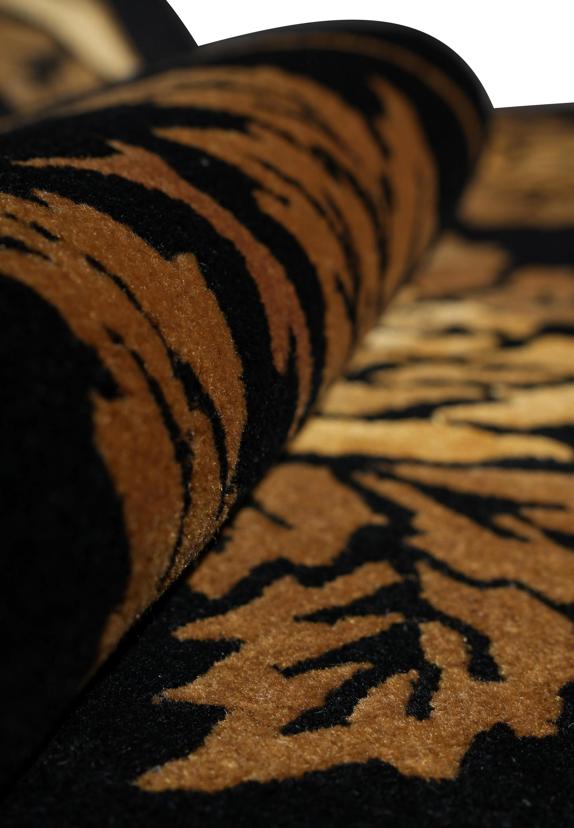 Rolled view of handmade black floral rug highlighting wool texture and raised design