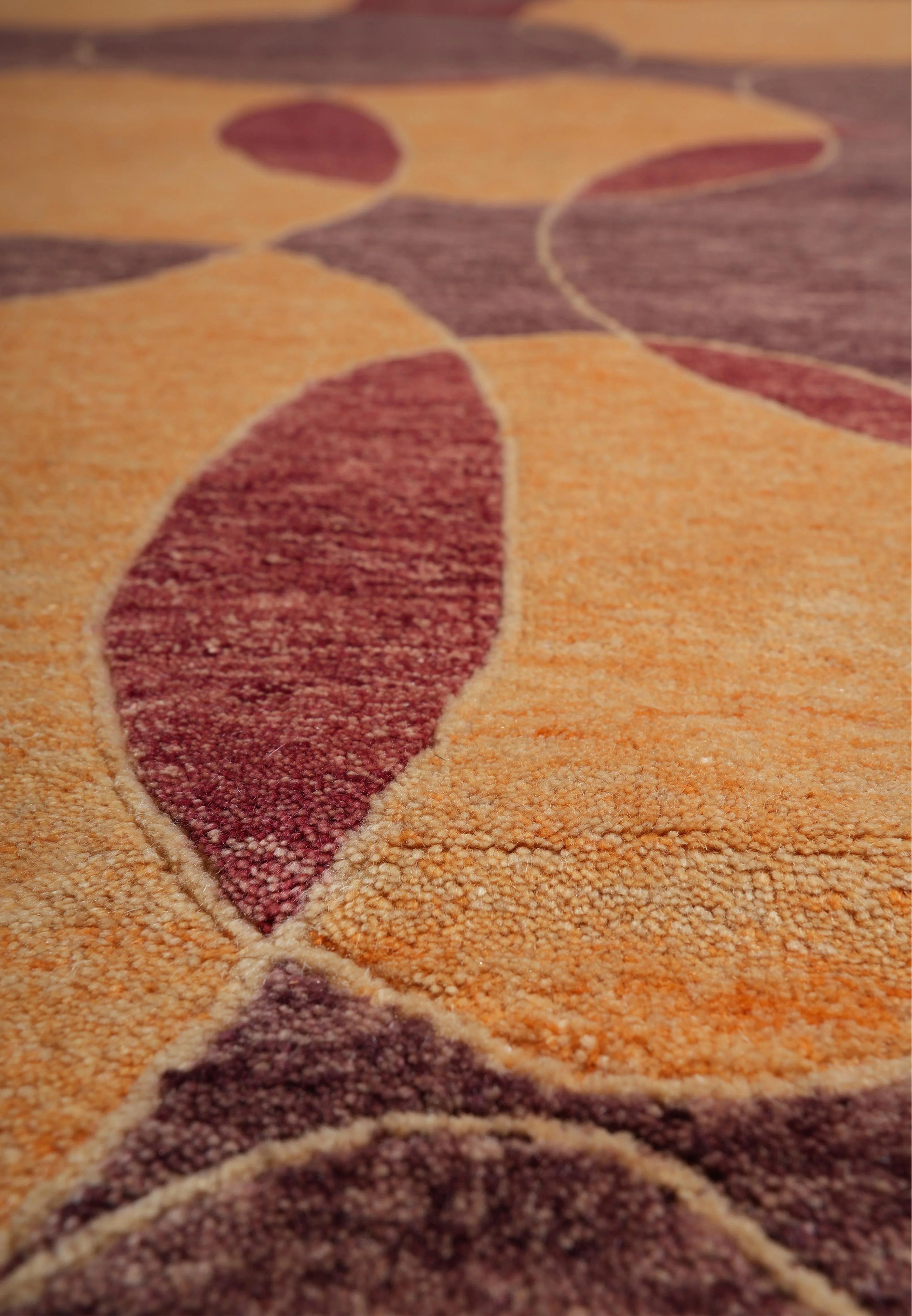 Closeup of the hand-knotted wool surface showing fine texture, smooth gradient transitions between amber and plum, and tactile carved outlines defining the modern circular motifs.
