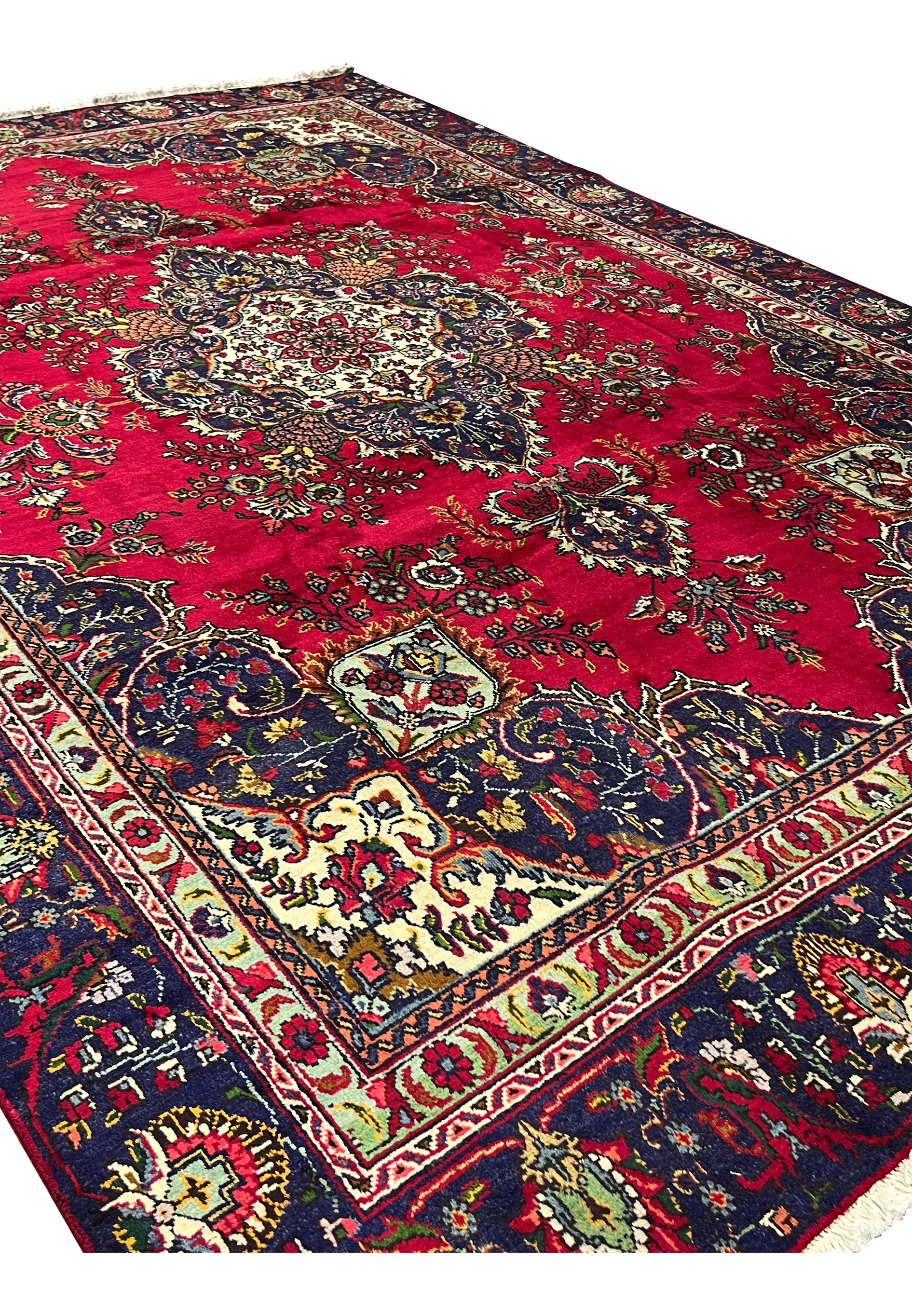 Angled view of 8'5" x 12'9" Persian Tabriz rug showing red field and navy corners