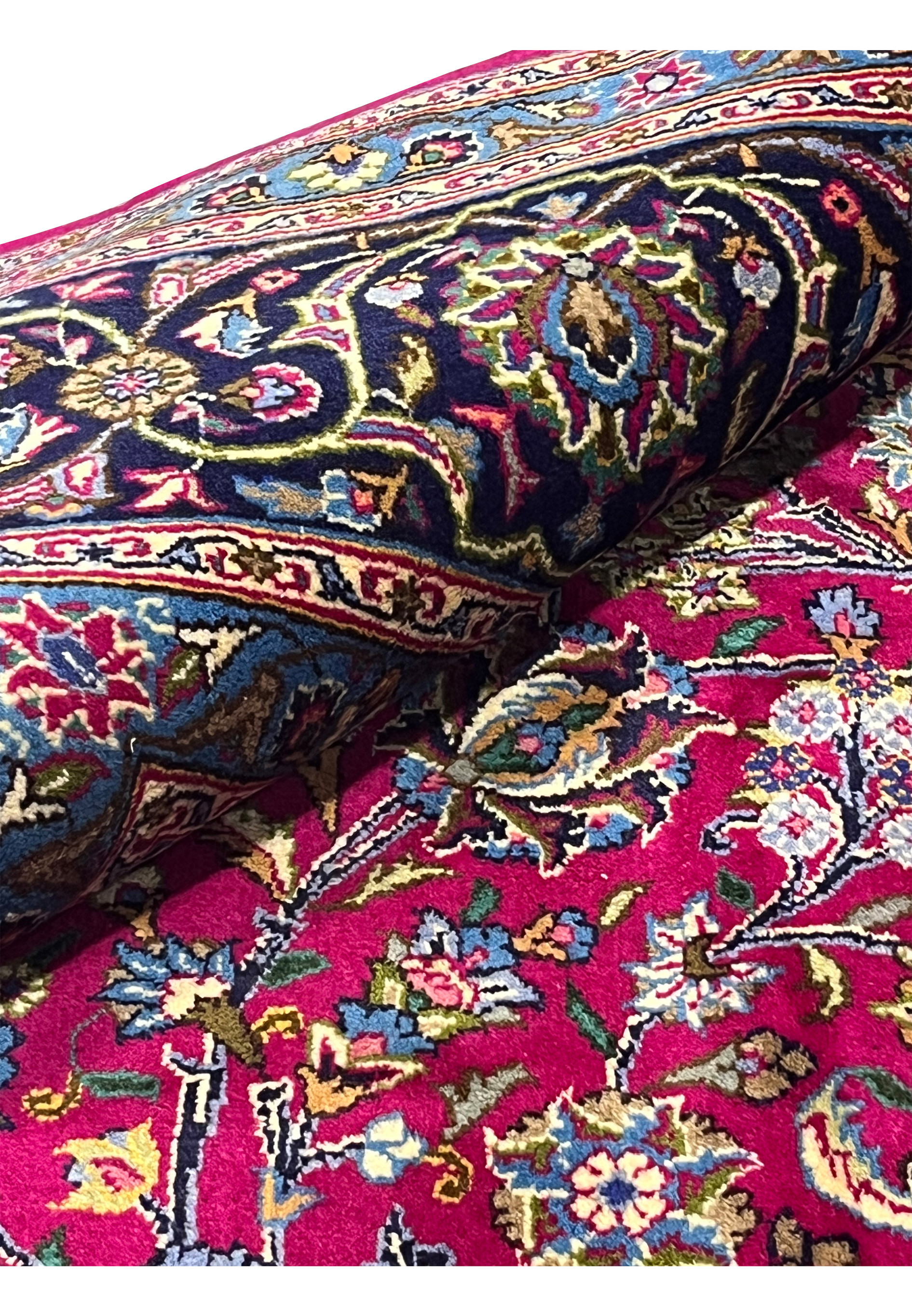 Rolled view of semi-antique Mashad rug highlighting red field, navy border, and intricate floral motifs.