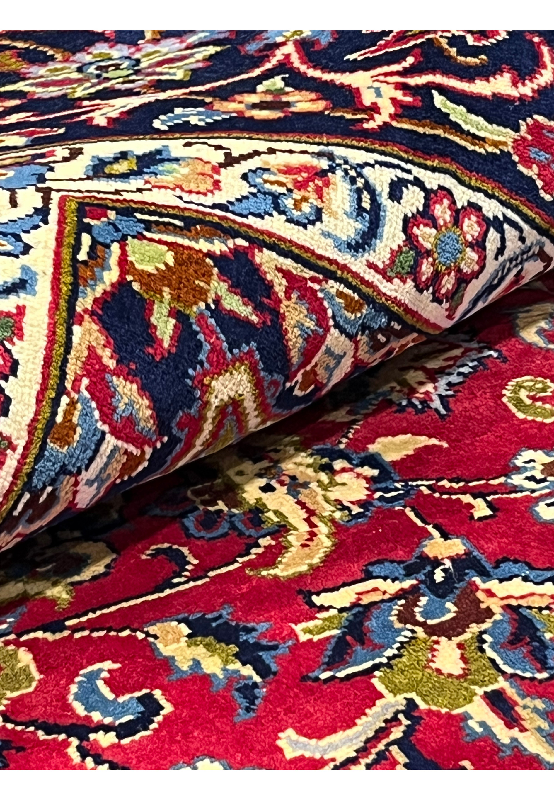 Rolled view of 8'5 x 11'8 Persian Isfahan rug showing fine wool pile, navy border, and floral patterns.