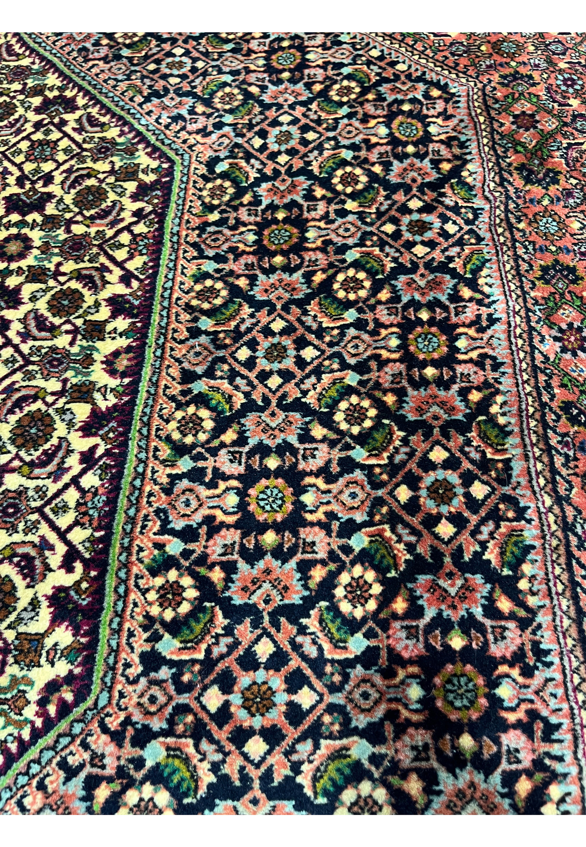 Detailed shot of small repeating Bijar floral motifs in navy, brick red, soft green, and ivory arranged in a tight lattice.