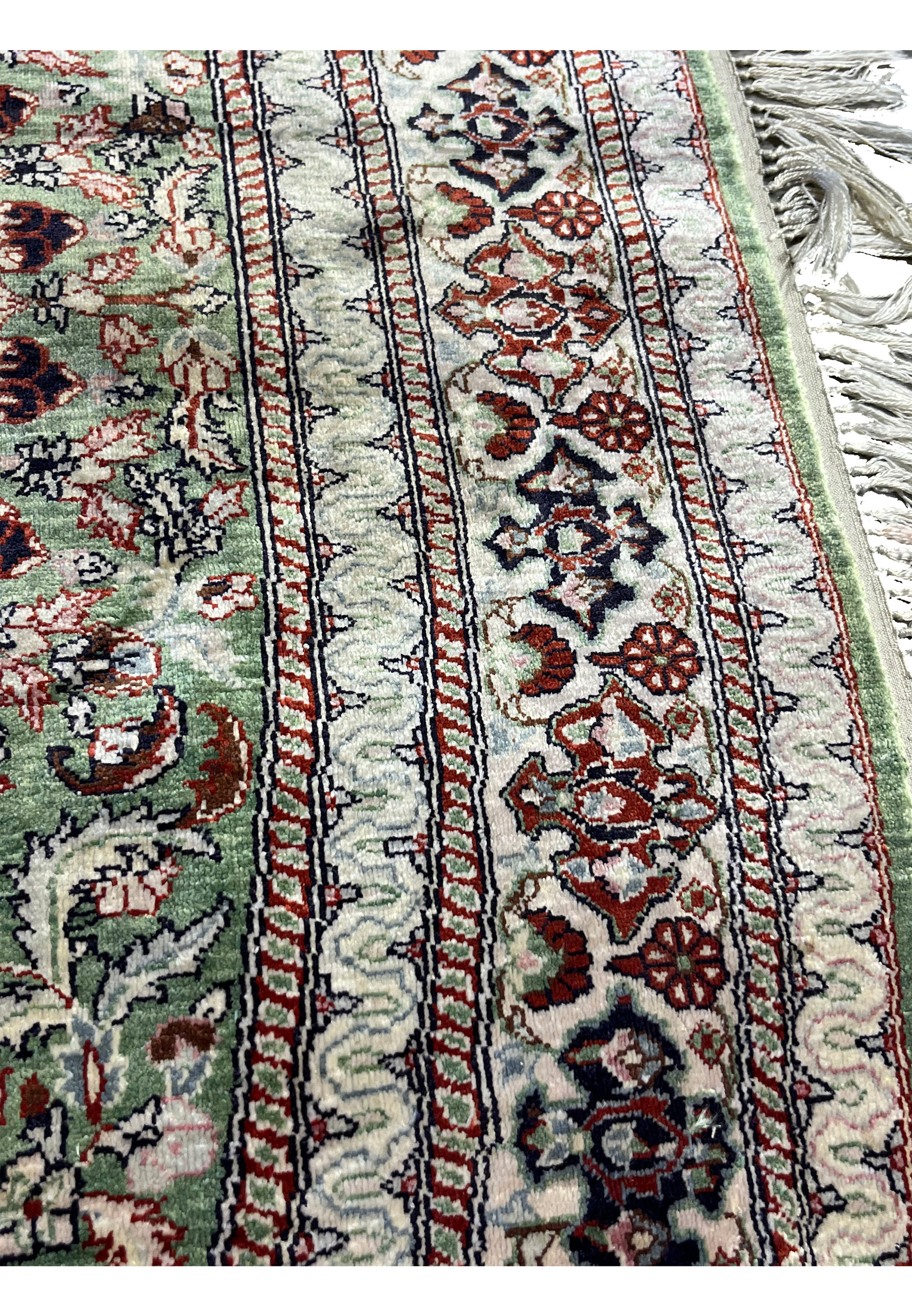 Border close-up of Qum pure silk rug showing layered floral bands, ivory and green tones, and delicate curvilinear motifs.