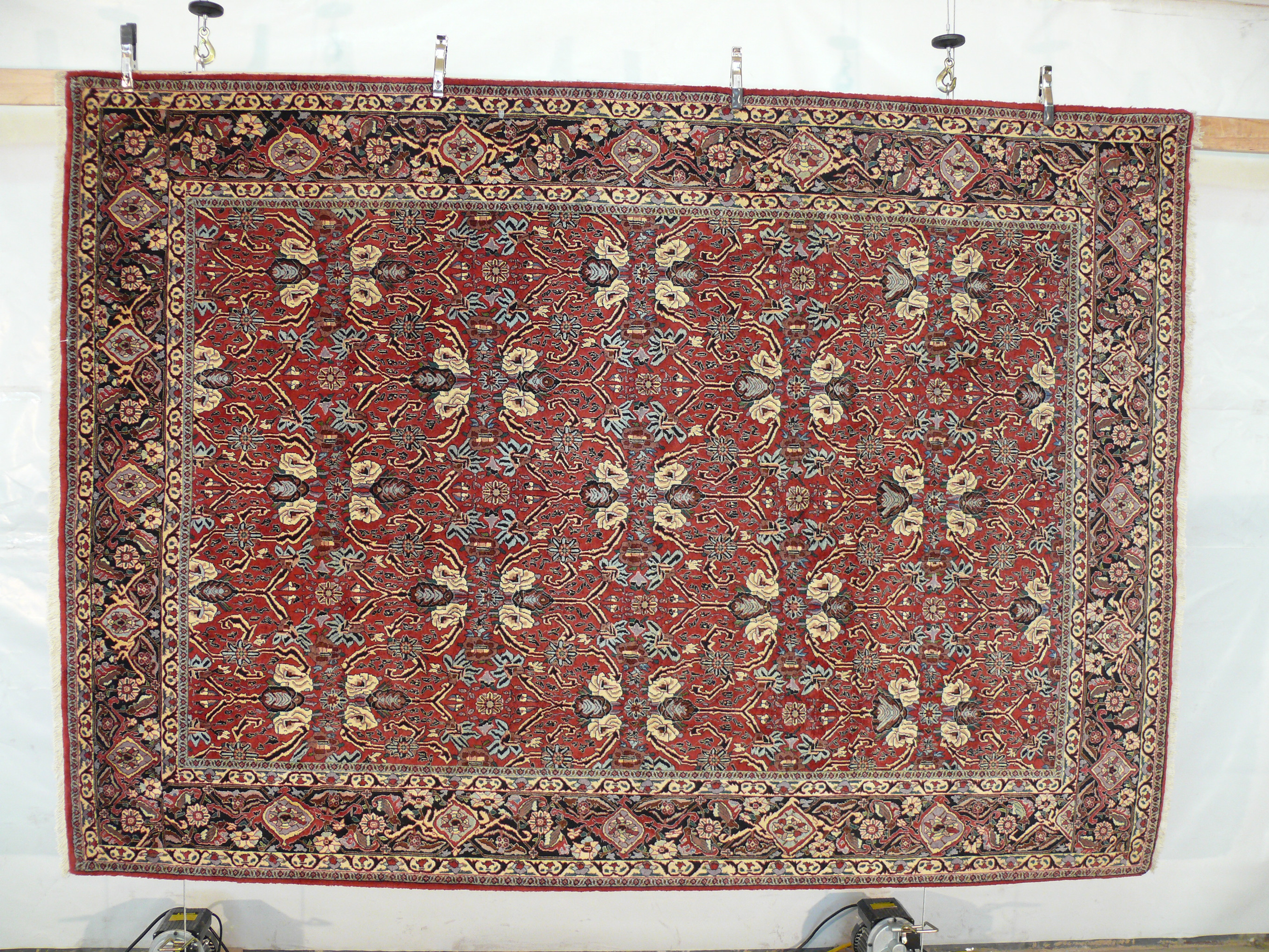 Hanging view of floral Bijar iron rug showing brick red background, ivory palmettes, navy vines, and dense wool texture