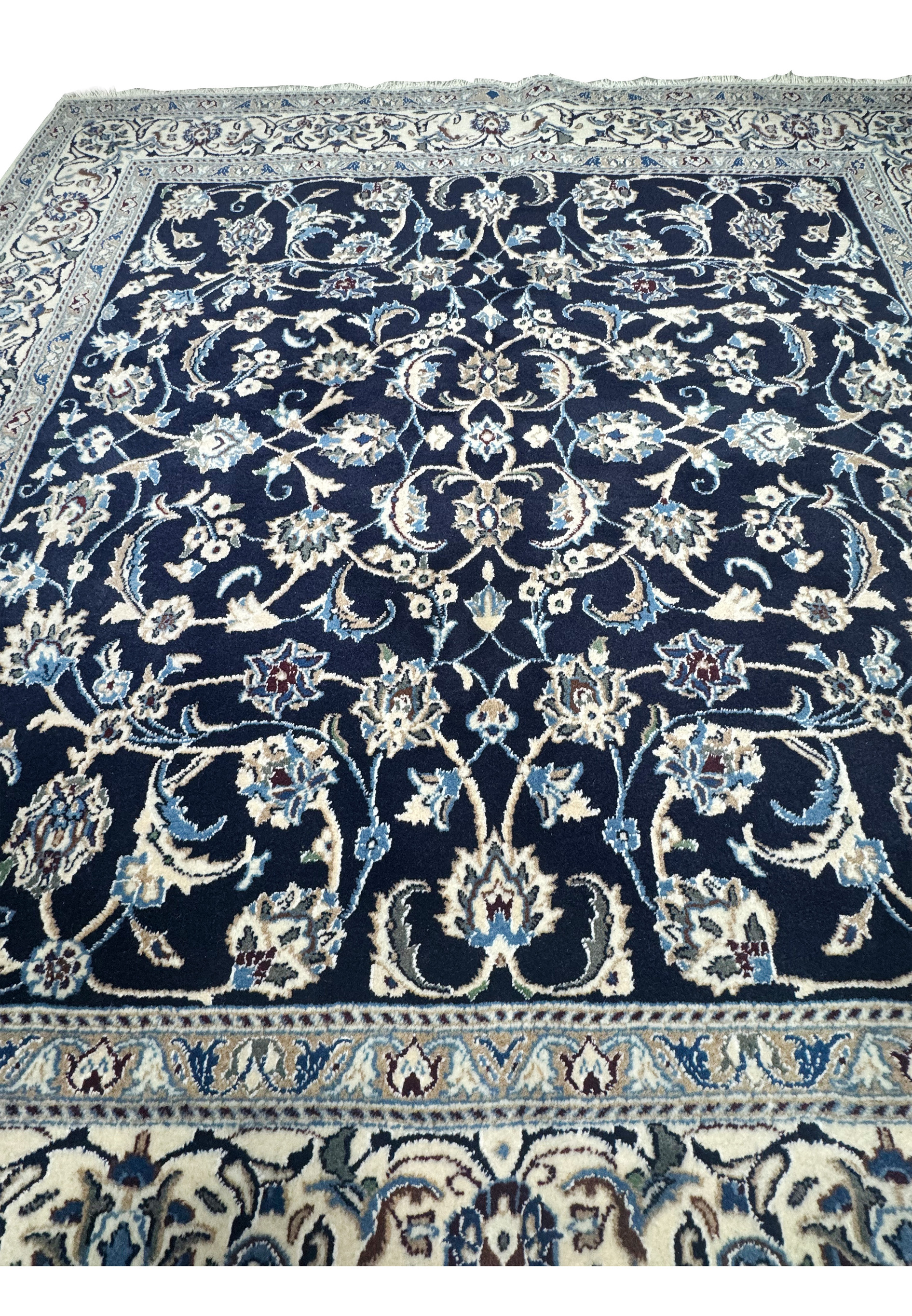 Midfield closeup of Persian Nain rug showing detailed floral vines, palmettes, and layered botanical motifs on navy background