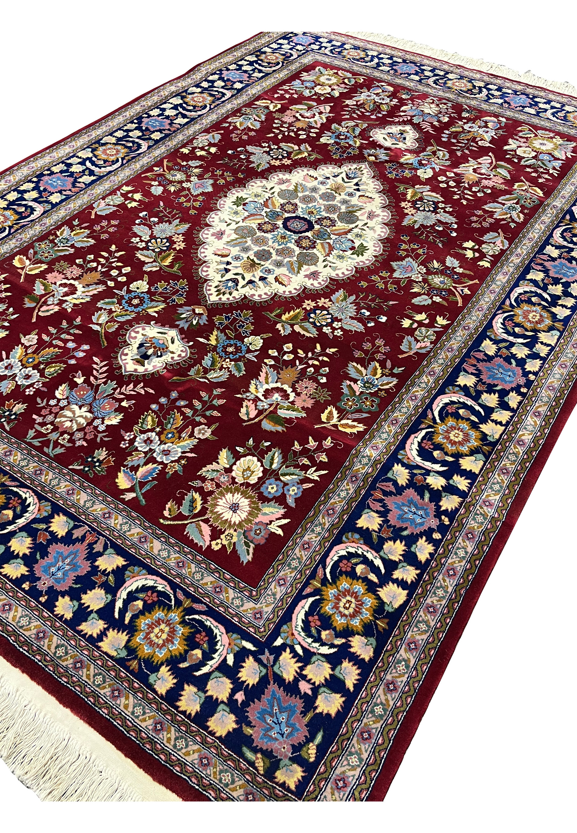 Angled view of Persian Isfahan wool and silk rug showing burgundy field, ivory medallion, and navy floral border