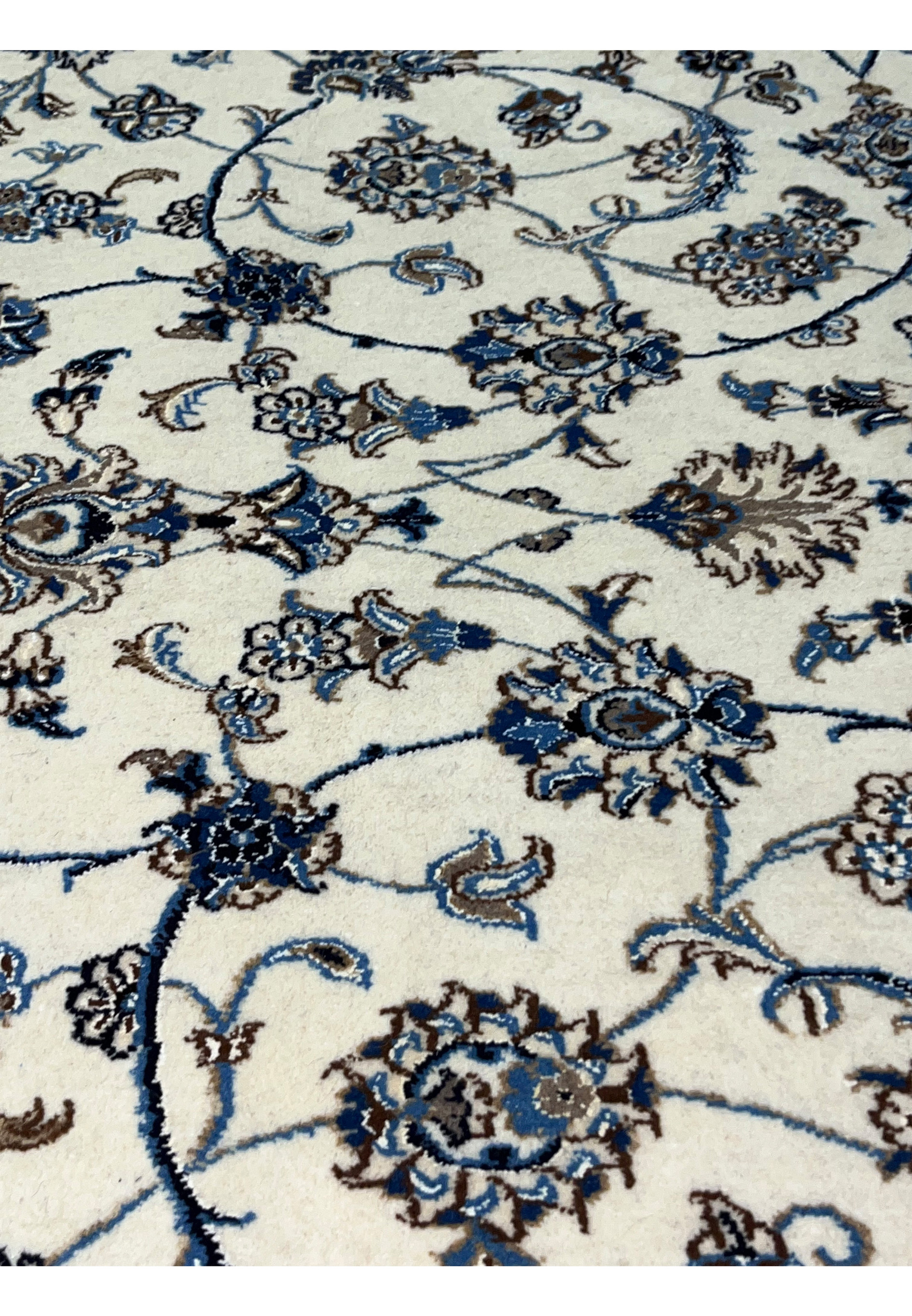 Close-up of ivory field on Persian Nain 9 LA rug showing fine blue floral scrolls and silk highlights