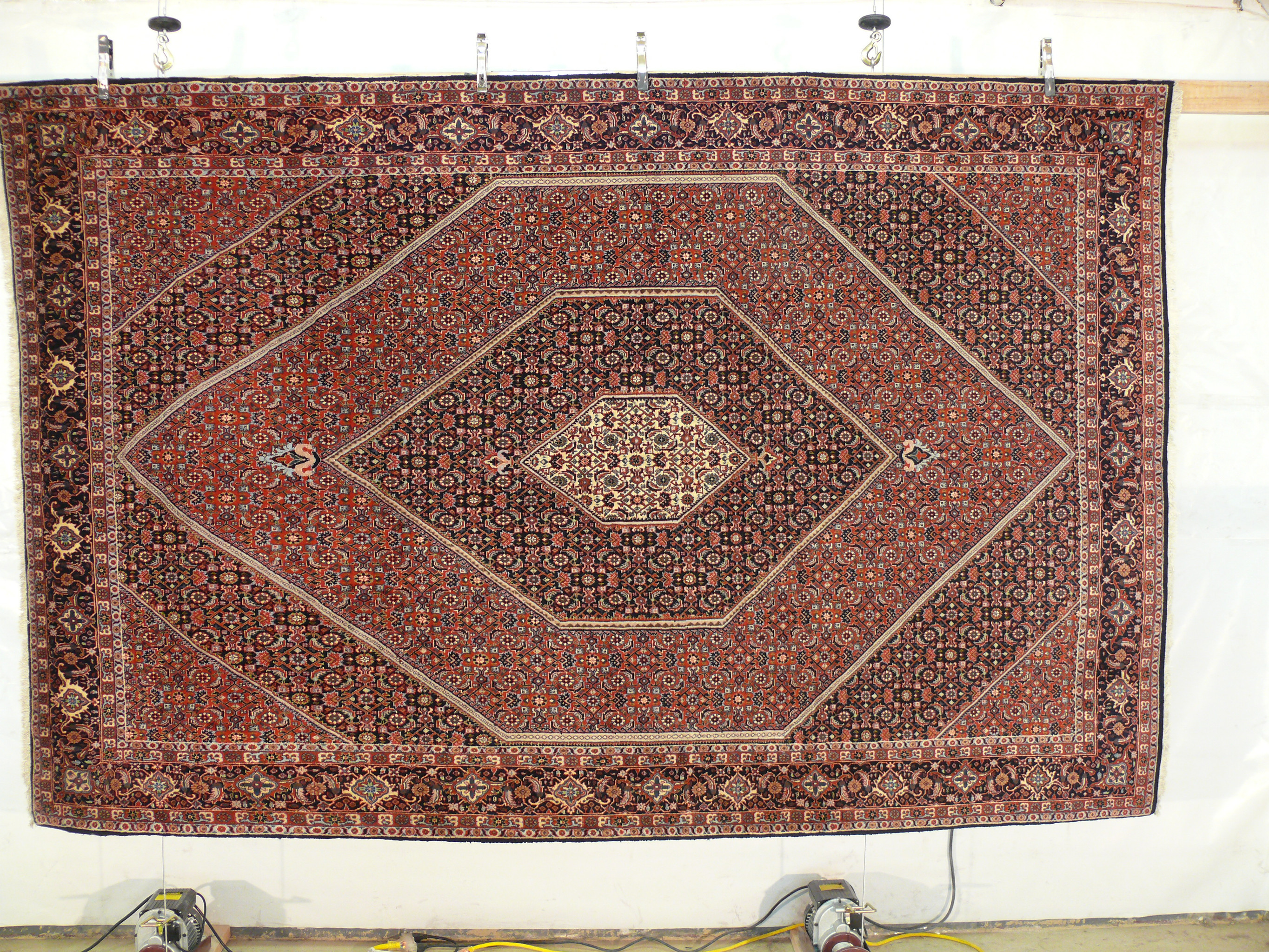 Large Bijar Persian iron rug hanging vertically showing full geometric medallion layout and detailed border pattern
