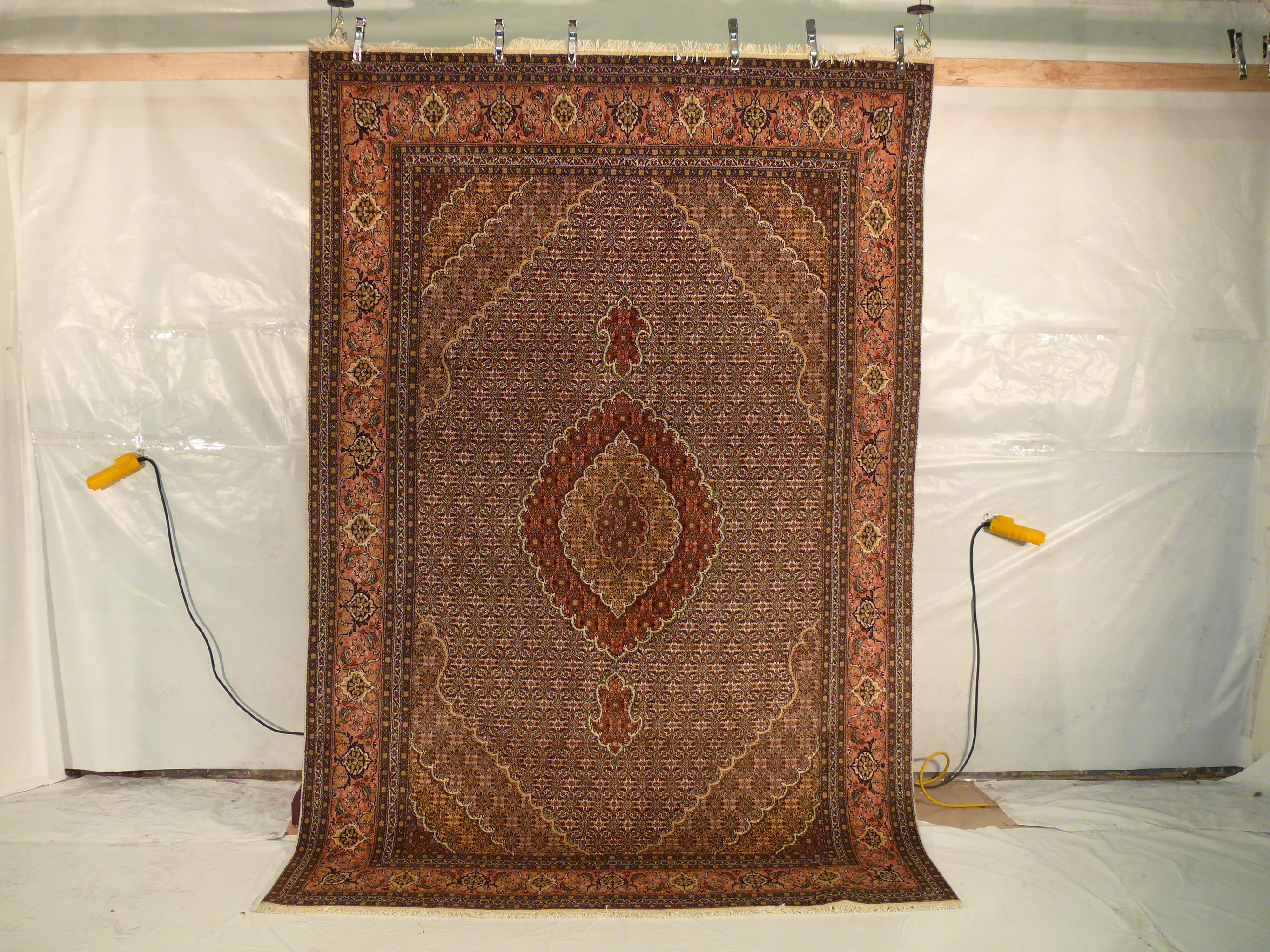 6'6 x 10 Persian Tabriz Mahi rug hanging view with dense Herati pattern and warm rust brown tones