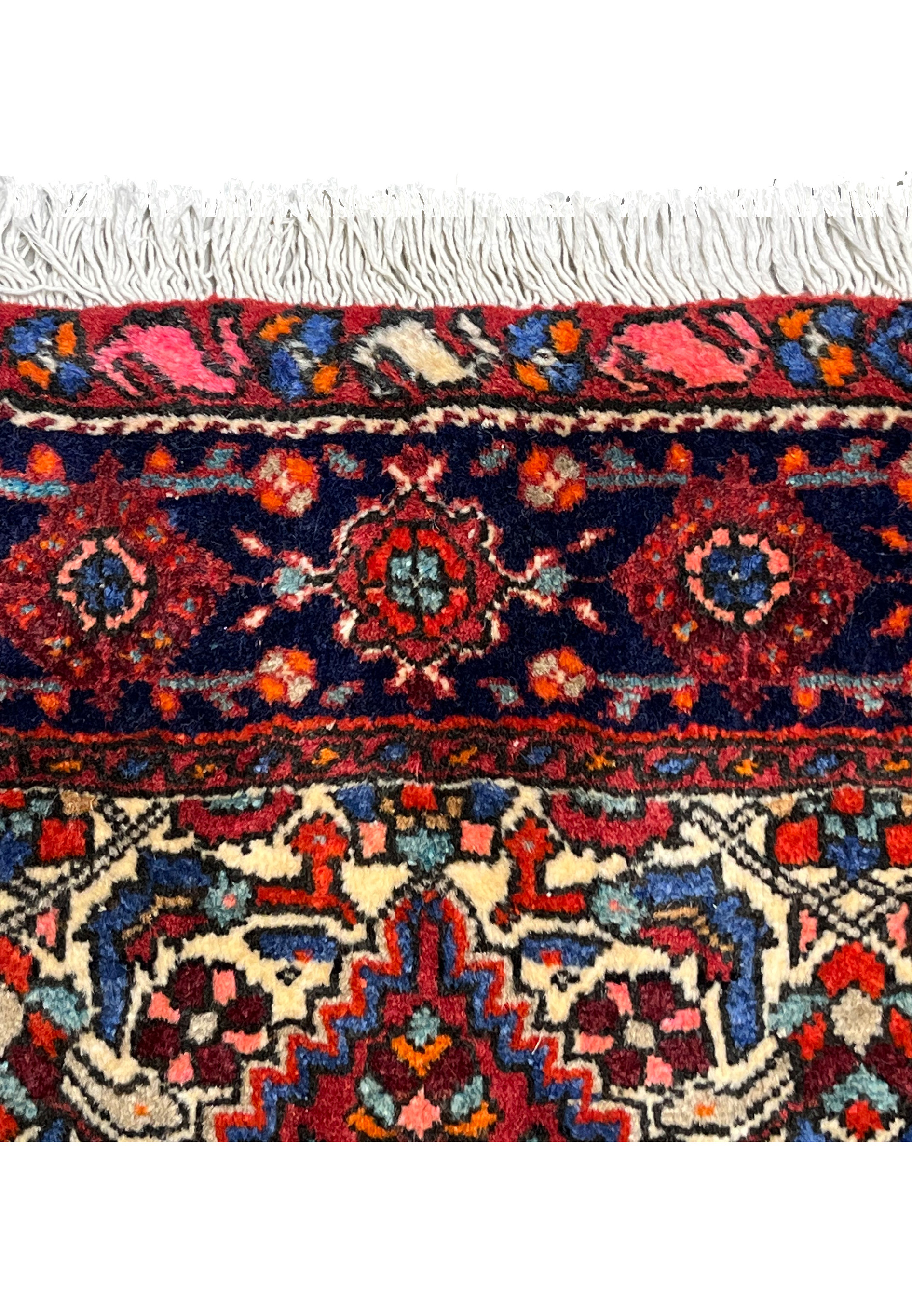 Upper border detail of a 3'4 x 4'9 Persian Gholtogh rug with dark navy border, geometric rosettes, rich reds, and hand-knotted wool fringe