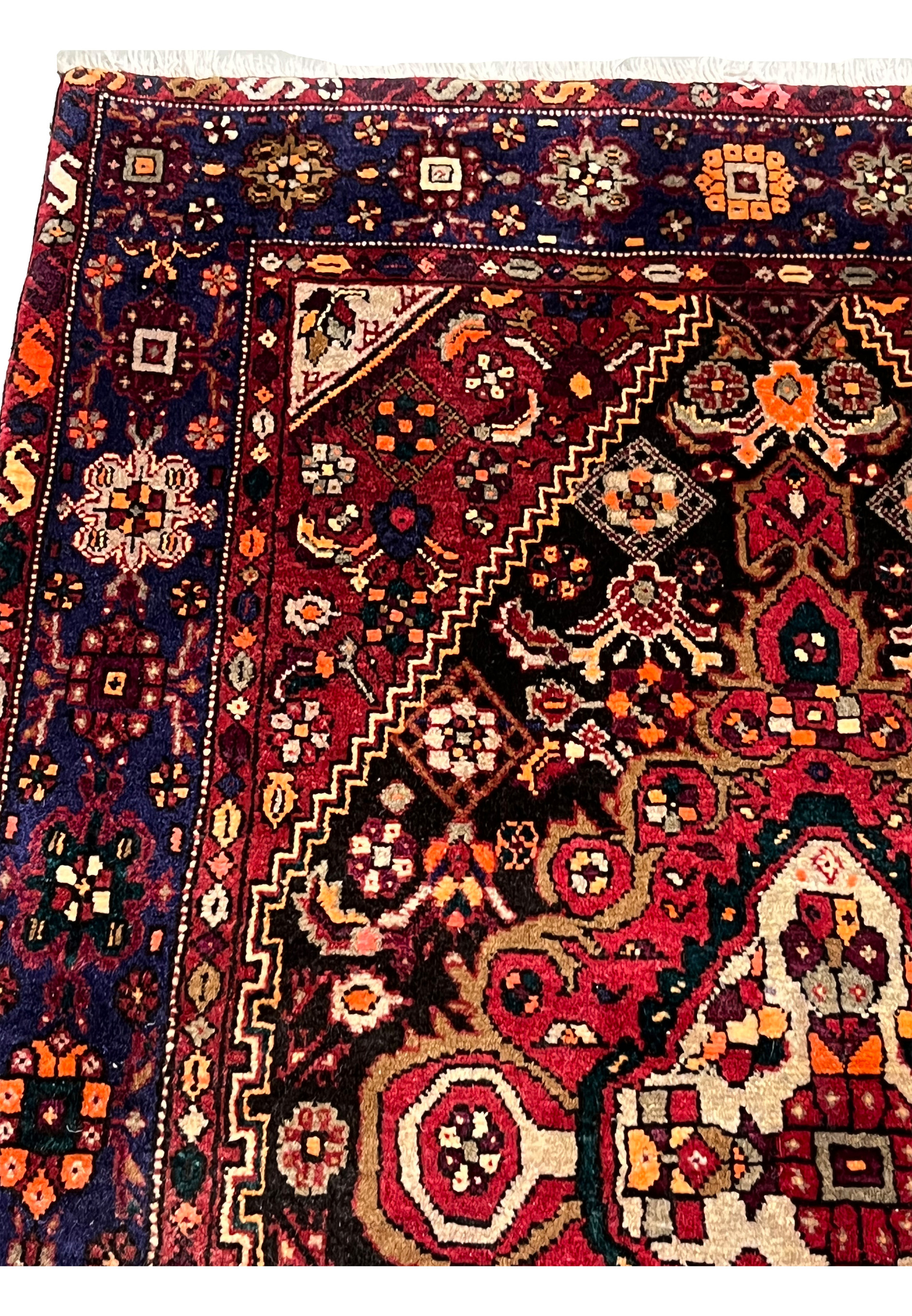 Upper border detail of a Persian Gholtogh rug featuring navy ground, repeating tribal motifs, geometric blossoms, and strong color contrast
