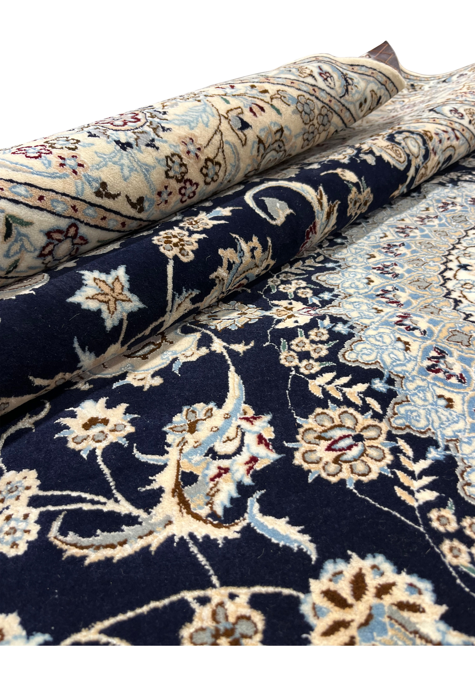 Rolled view of a handmade Persian Nain 6LA rug showing thickness, flexibility, and contrasting navy field against ivory border while partially rolled