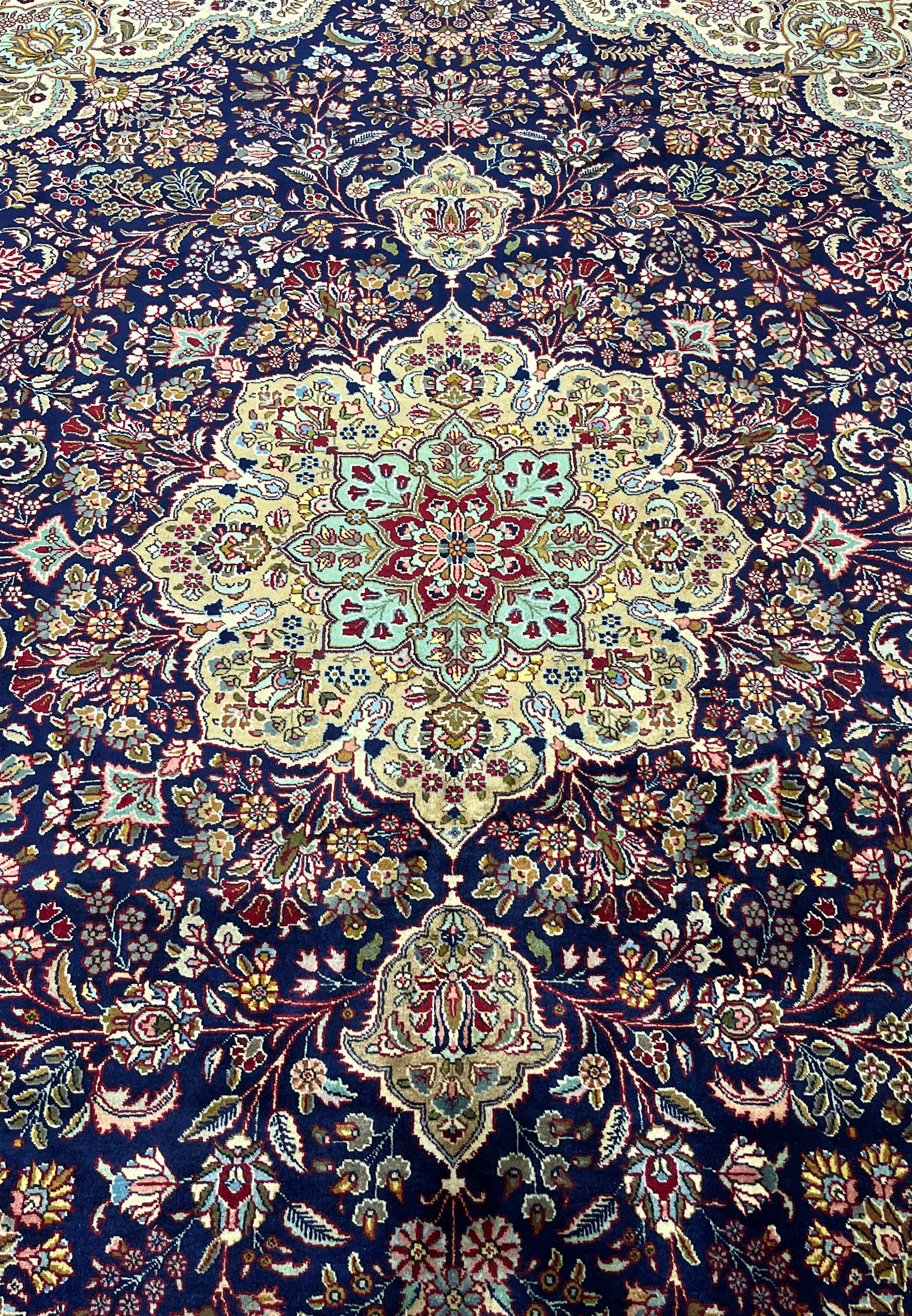 Central medallion of Persian Tabriz rug with ivory, light blue, burgundy, and gold tones set on a deep navy background