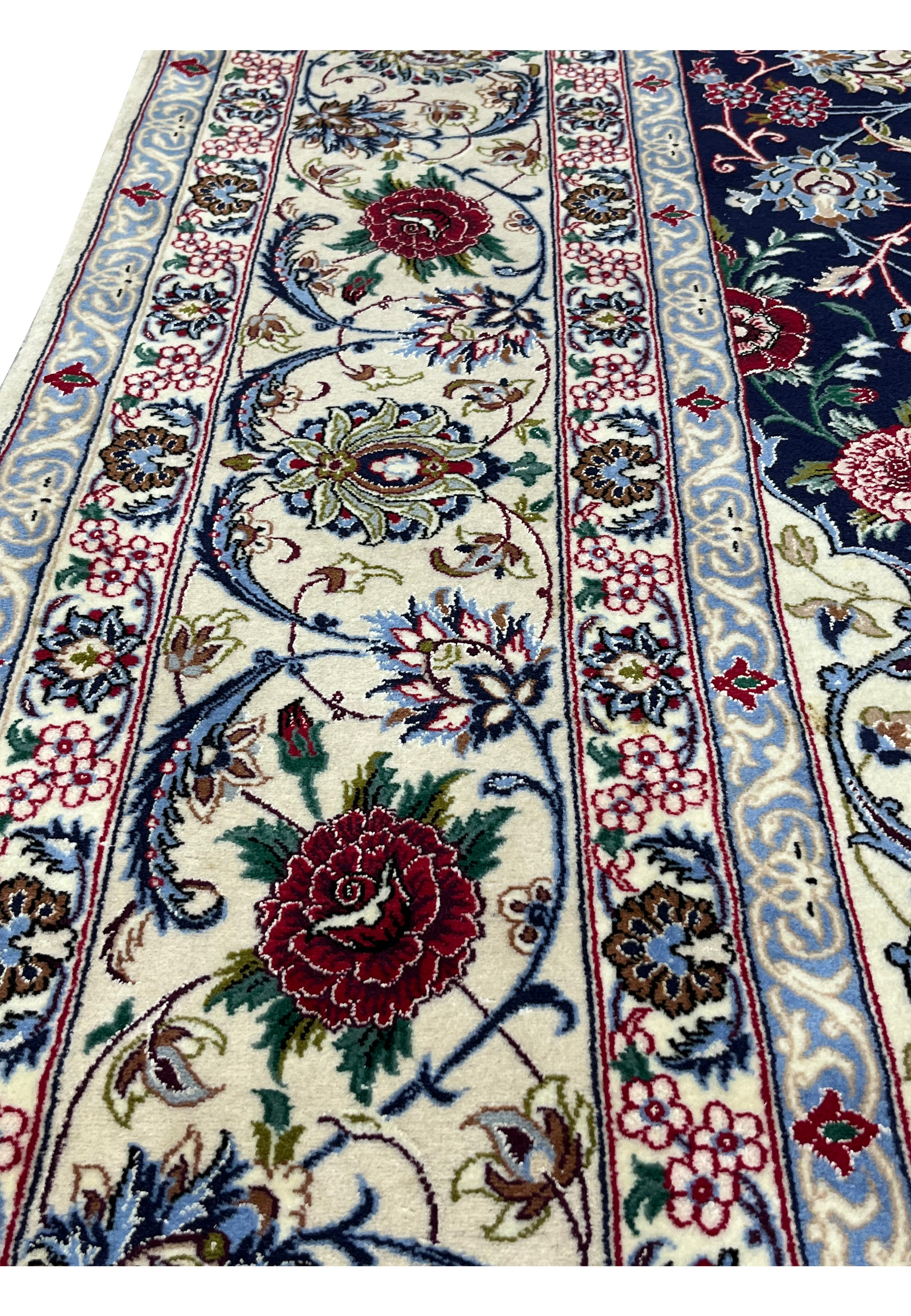 Border close-up of a Persian Isfahan rug revealing intricate floral motifs in ivory, light blue, burgundy, olive, and navy with silk highlights