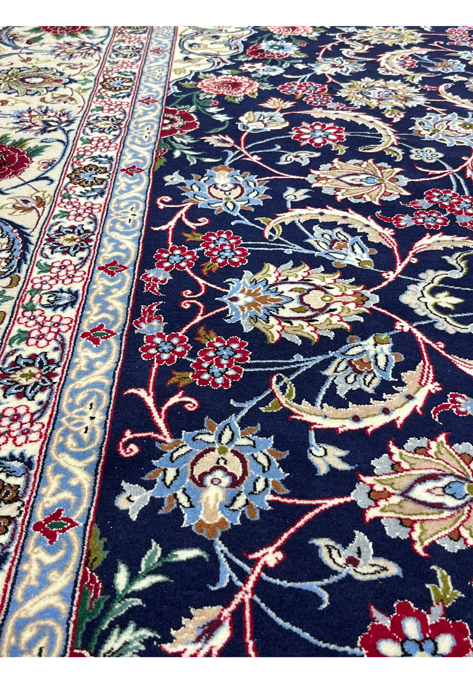 Detailed view of Persian Isfahan rug motifs featuring flowing floral patterns in navy blue, ivory, burgundy, light blue, and soft gold