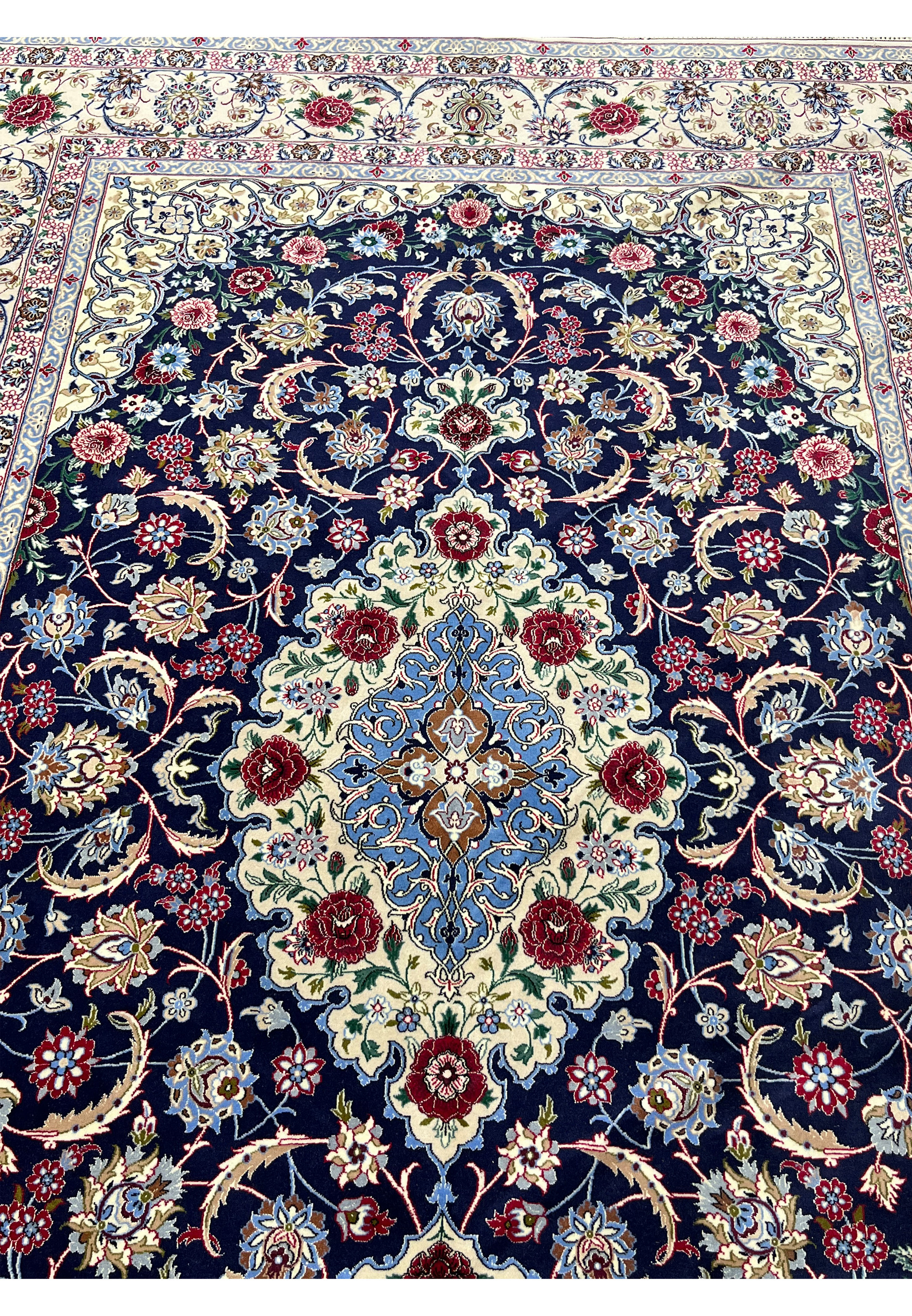 Top view of a 7x10 super fine Persian Isfahan rug with deep navy field, ivory medallion, red floral motifs, and detailed silk highlights