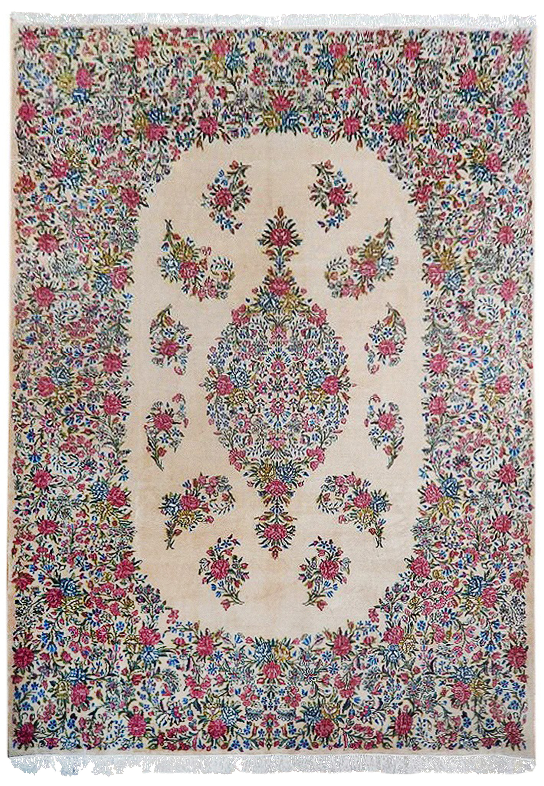 Straight-on image of a hand-knotted Persian Kerman rug featuring an ivory background, floral medallion, pastel pink flowers, and blue vine motifs