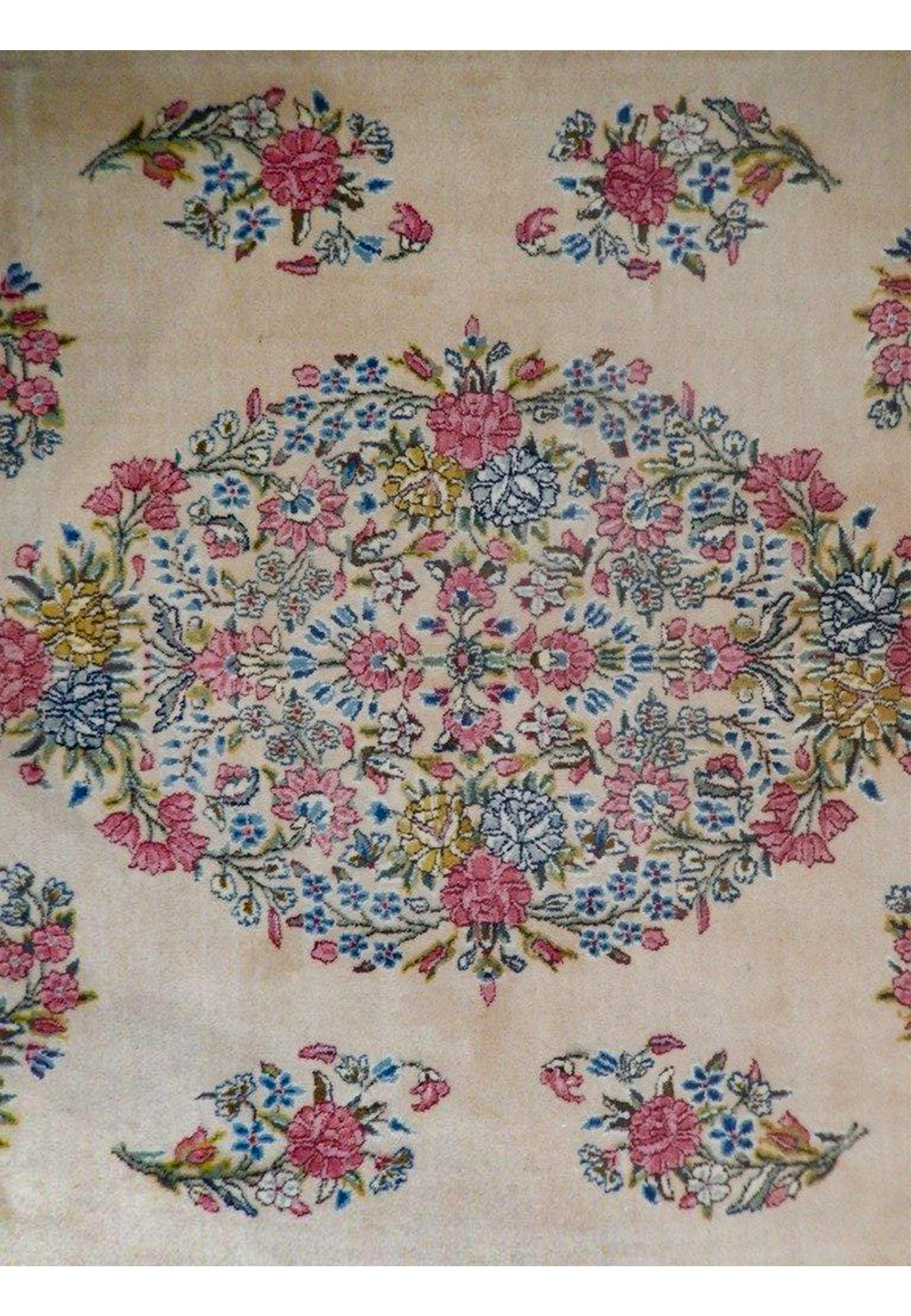 Close-up of the central medallion on a Persian Kerman rug showing layered floral clusters in pink, light blue, soft green, and pale yellow tones