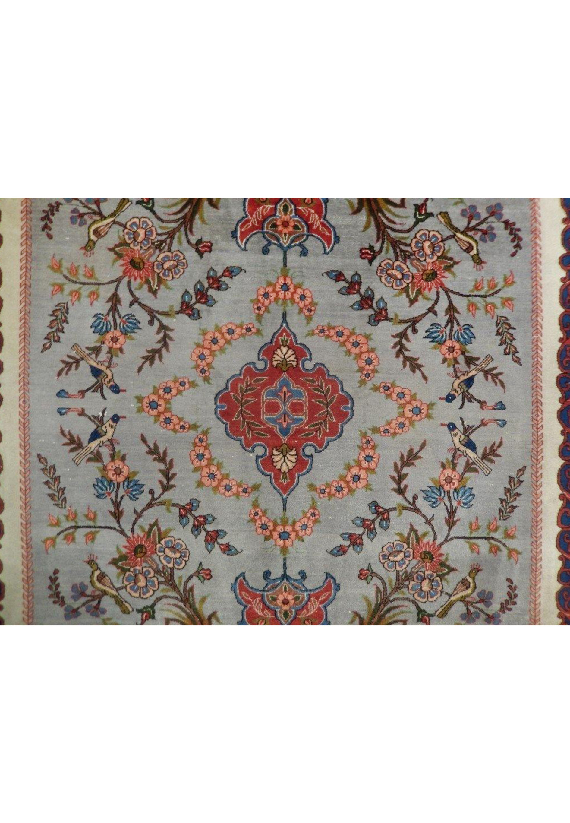 Close-up of the central medallion on a grey Persian Isfahan rug showing floral detailing, muted red tones, steel blue vines, and ivory outlines