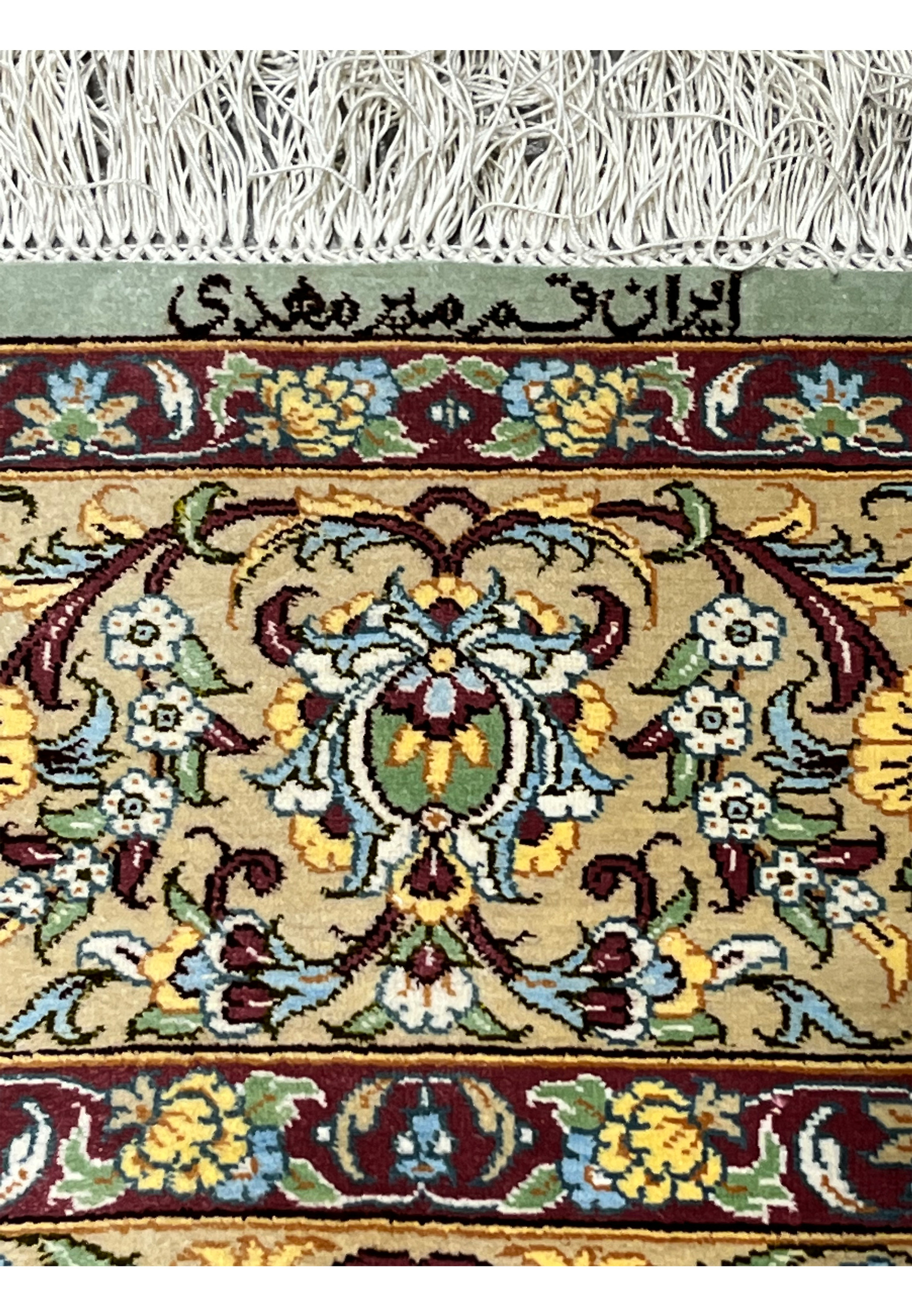 Zoomed detail of Mirmehdi signature woven in black silk at the end of a Persian Qum pure silk rug with ivory fringe
