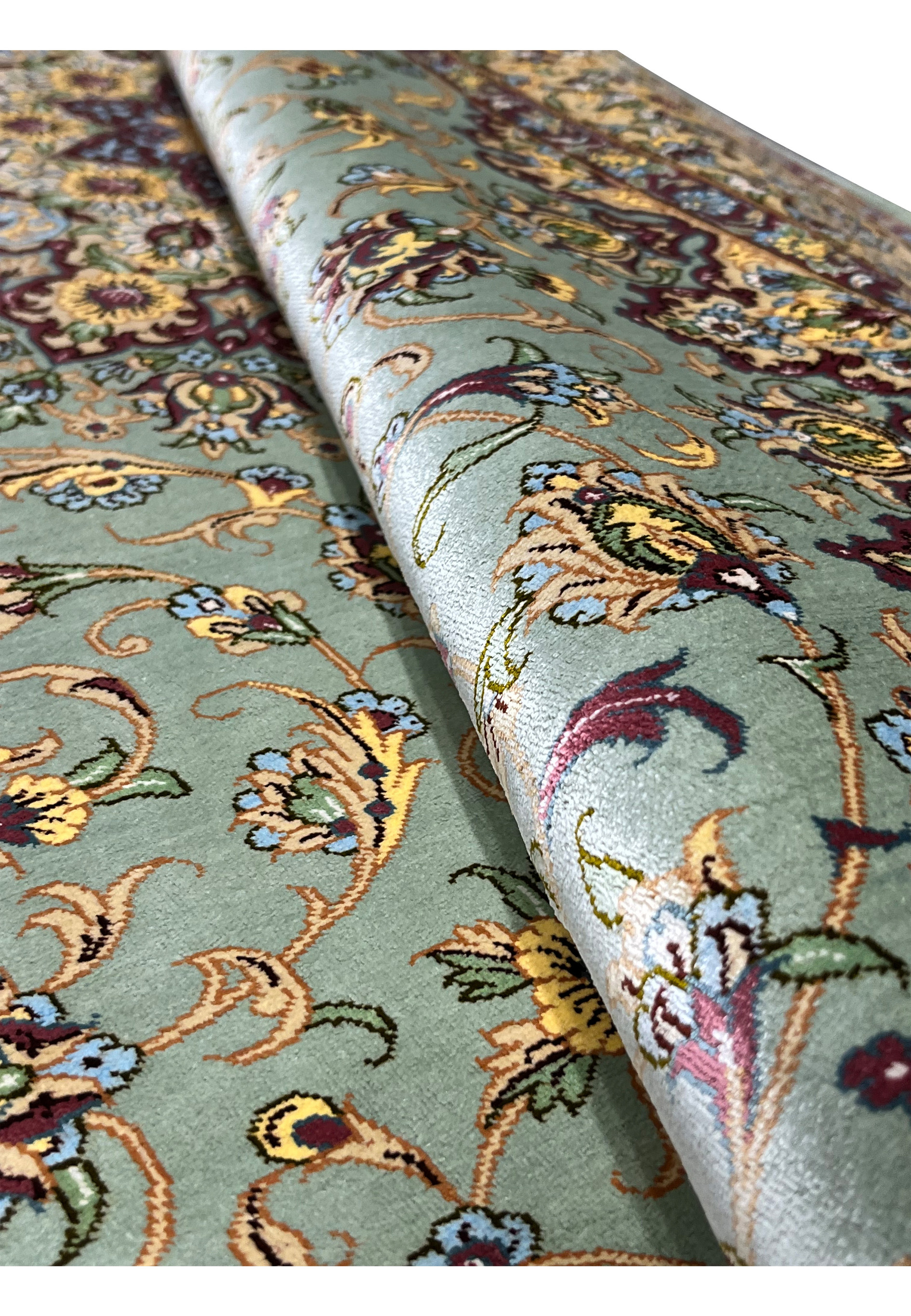 Rolled Persian Qum pure silk rug revealing fine silk pile sheen, dusty sage green field, and intricate floral pattern with burgundy and gold accents