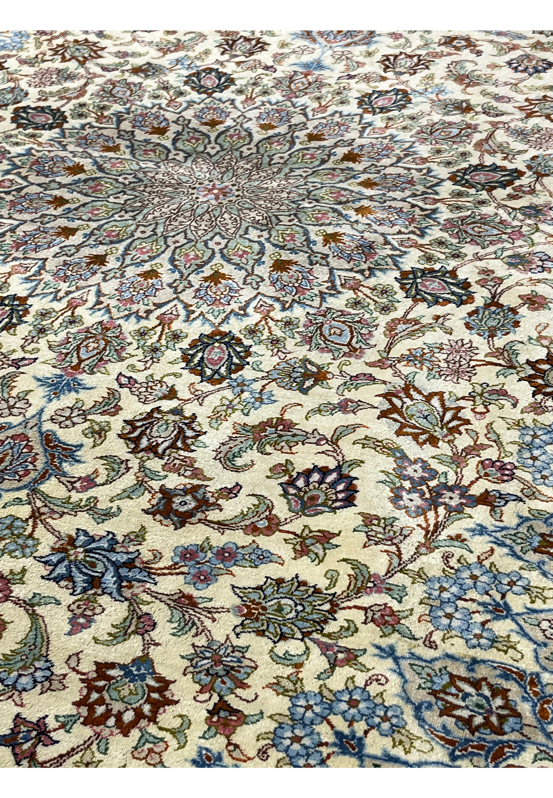 Detailed surface view of a Persian Qum pure silk rug displaying dense floral motifs, scrolling vines, and refined pastel colors on an ivory background.
