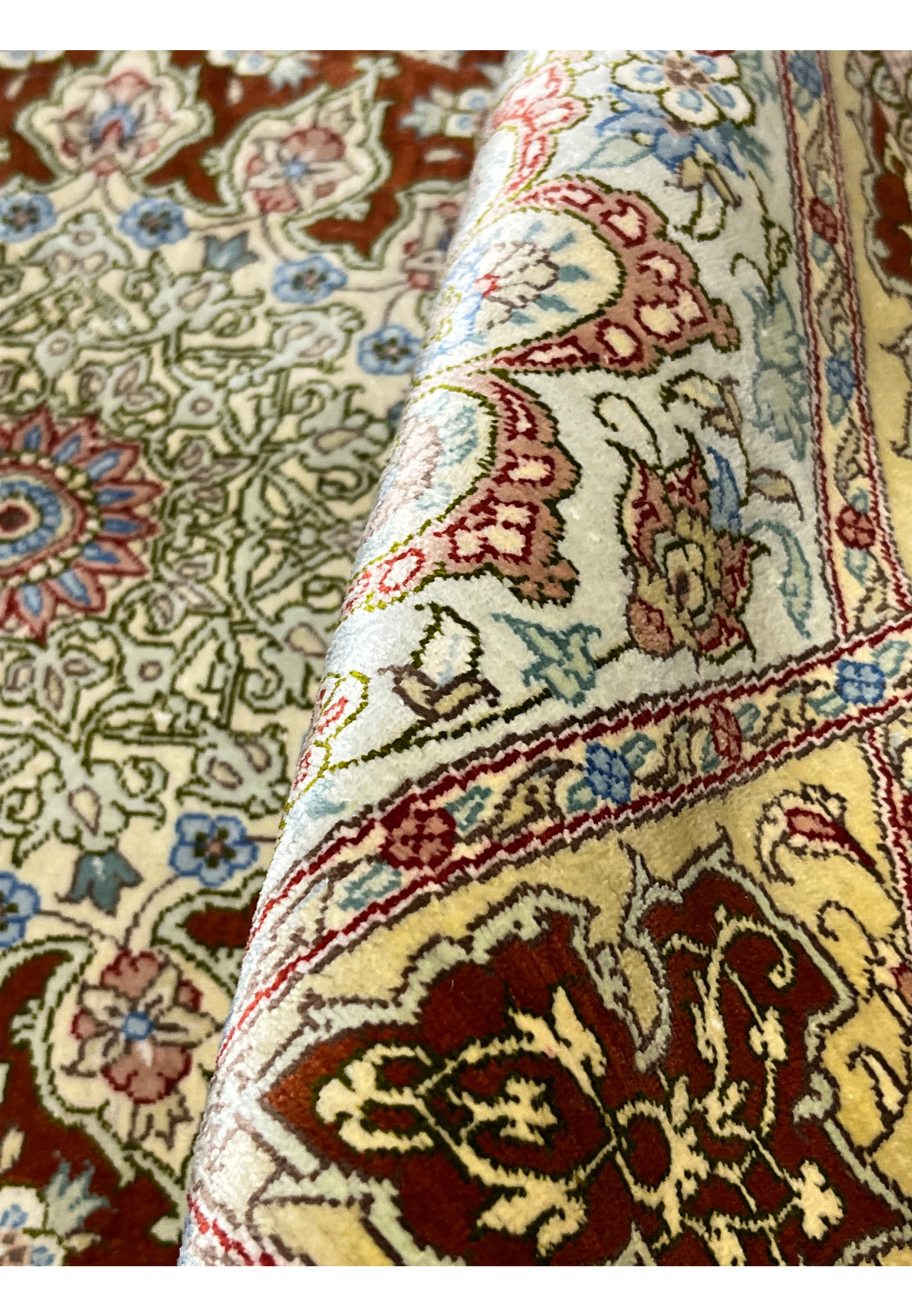 Rolled view of signed Amjadi Persian Qum silk on silk square rug demonstrating flexibility, refined weave, and smooth silk surface