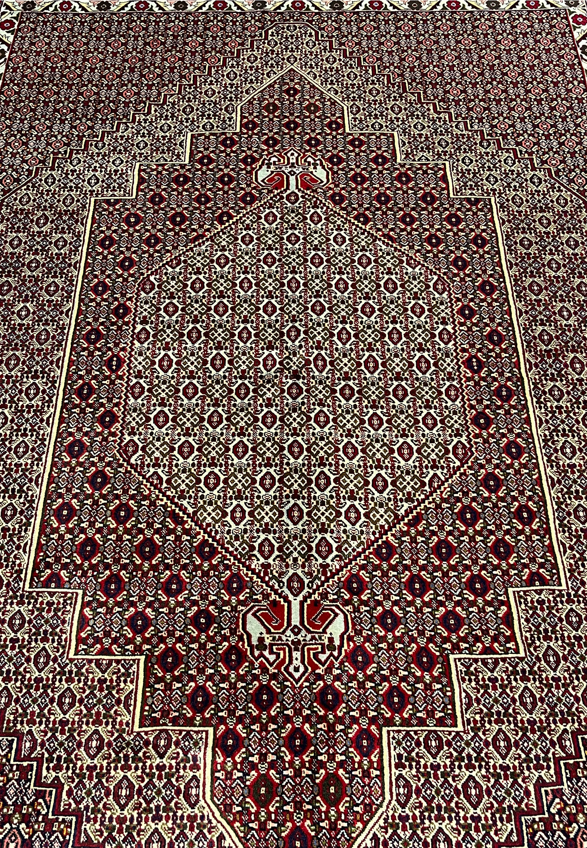 Central medallion detail of Persian Senneh rug with stepped diamond geometry, ivory framing, and dense burgundy and brown pattern fill.