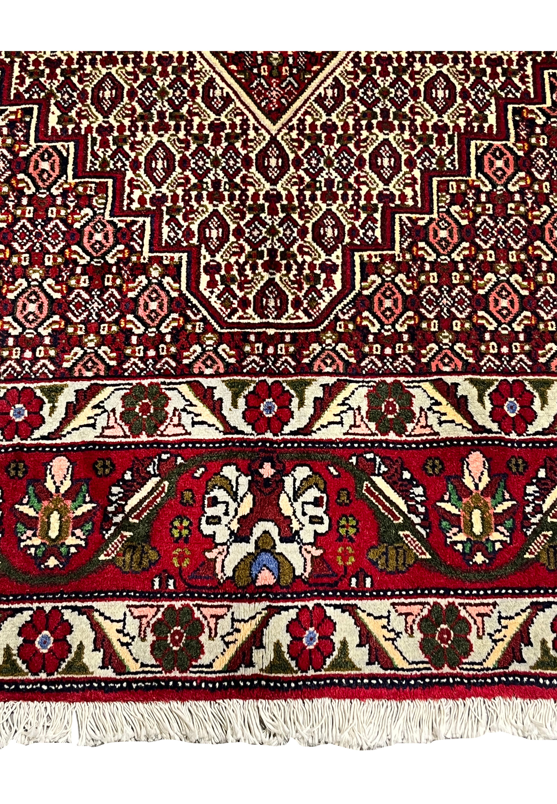 Lower border detail of Persian Senneh rug showing red ground, stylized floral motifs, ivory outlines, olive accents, and crisp geometric framing
