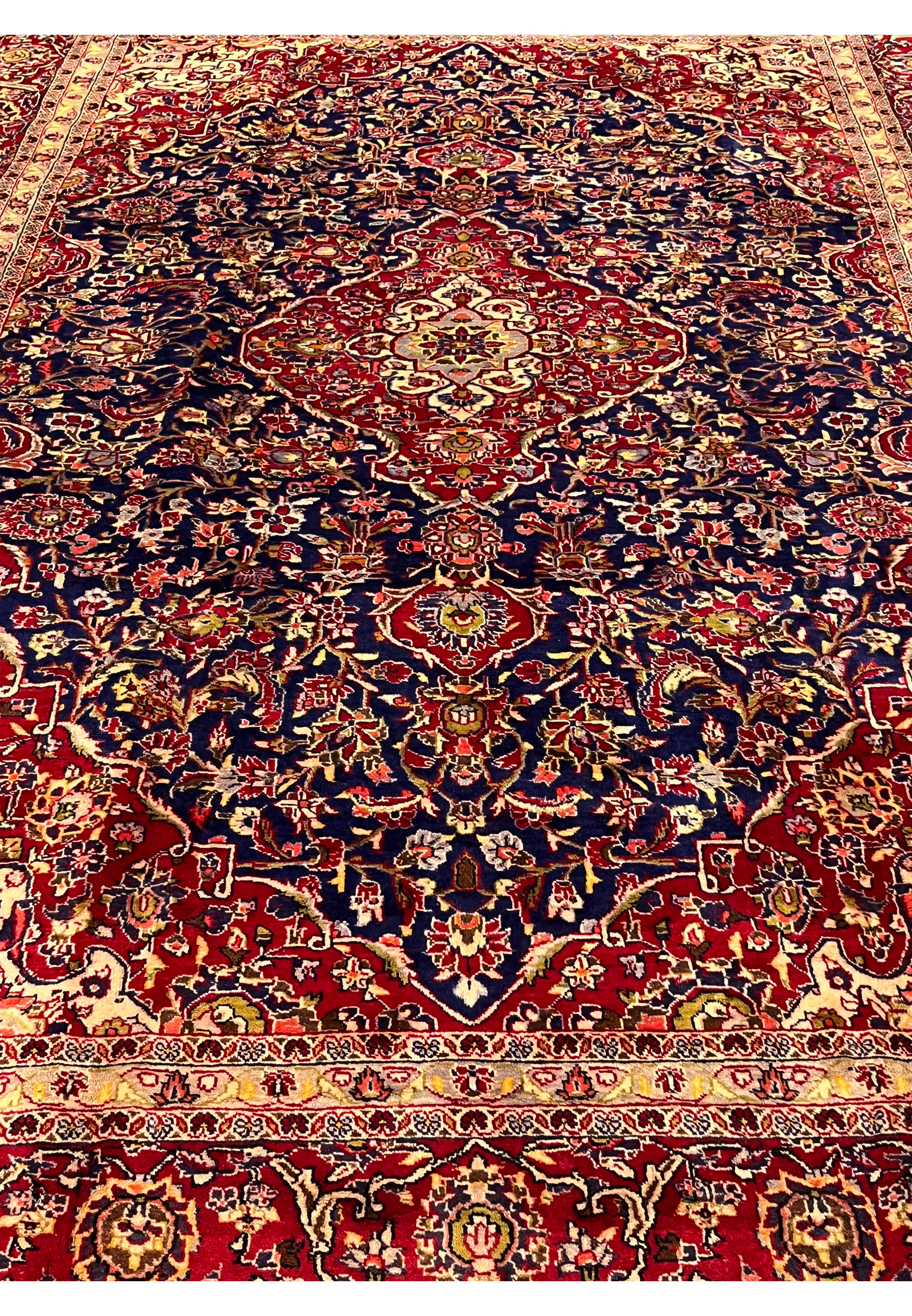 Top view of Persian Isfahan rug highlighting symmetrical floral composition, navy blue field, red medallion center, and ivory framing borders