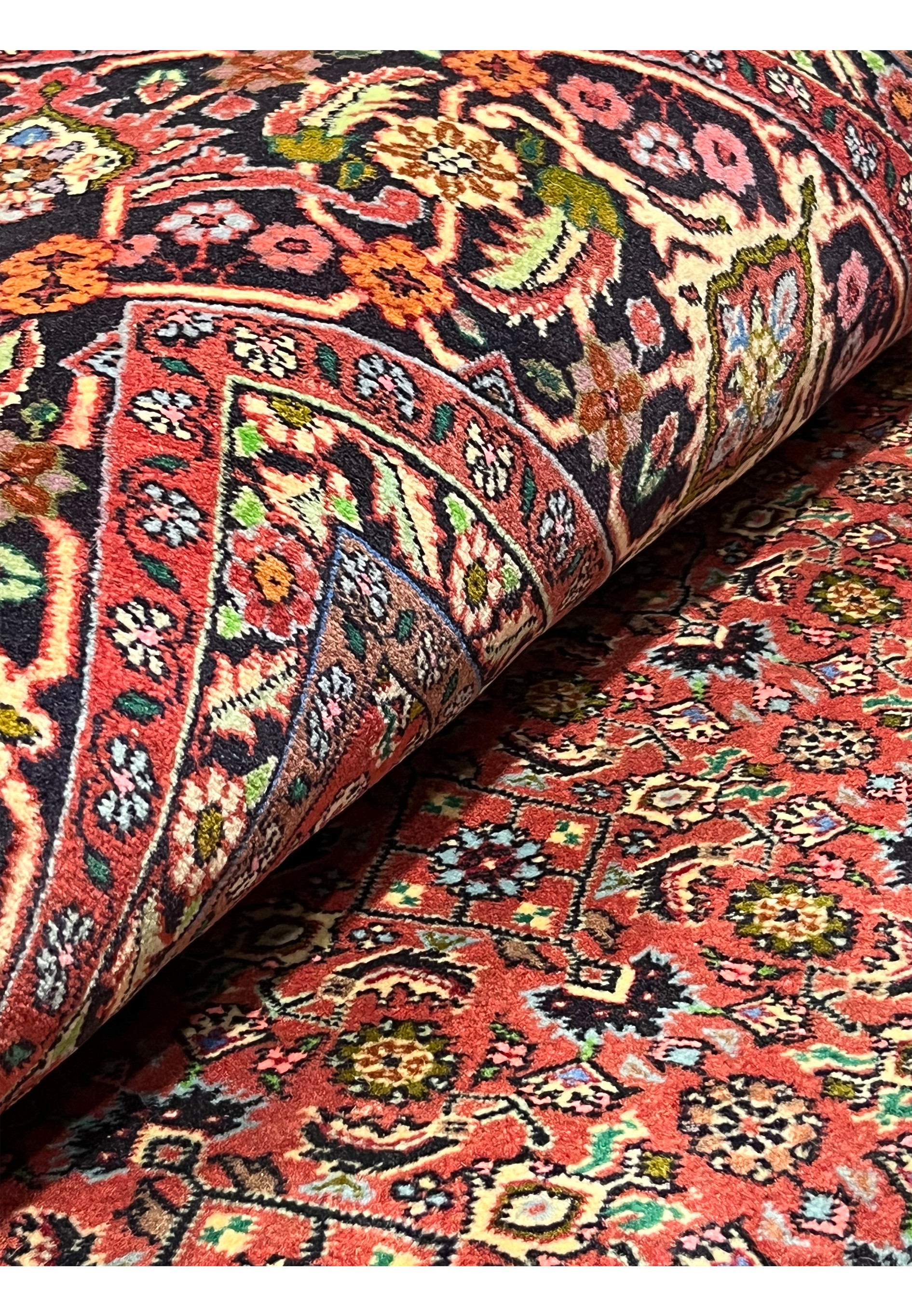 Persian Bijar all-over rug partially rolled to display rich terracotta field, navy border, and intricate floral motifs