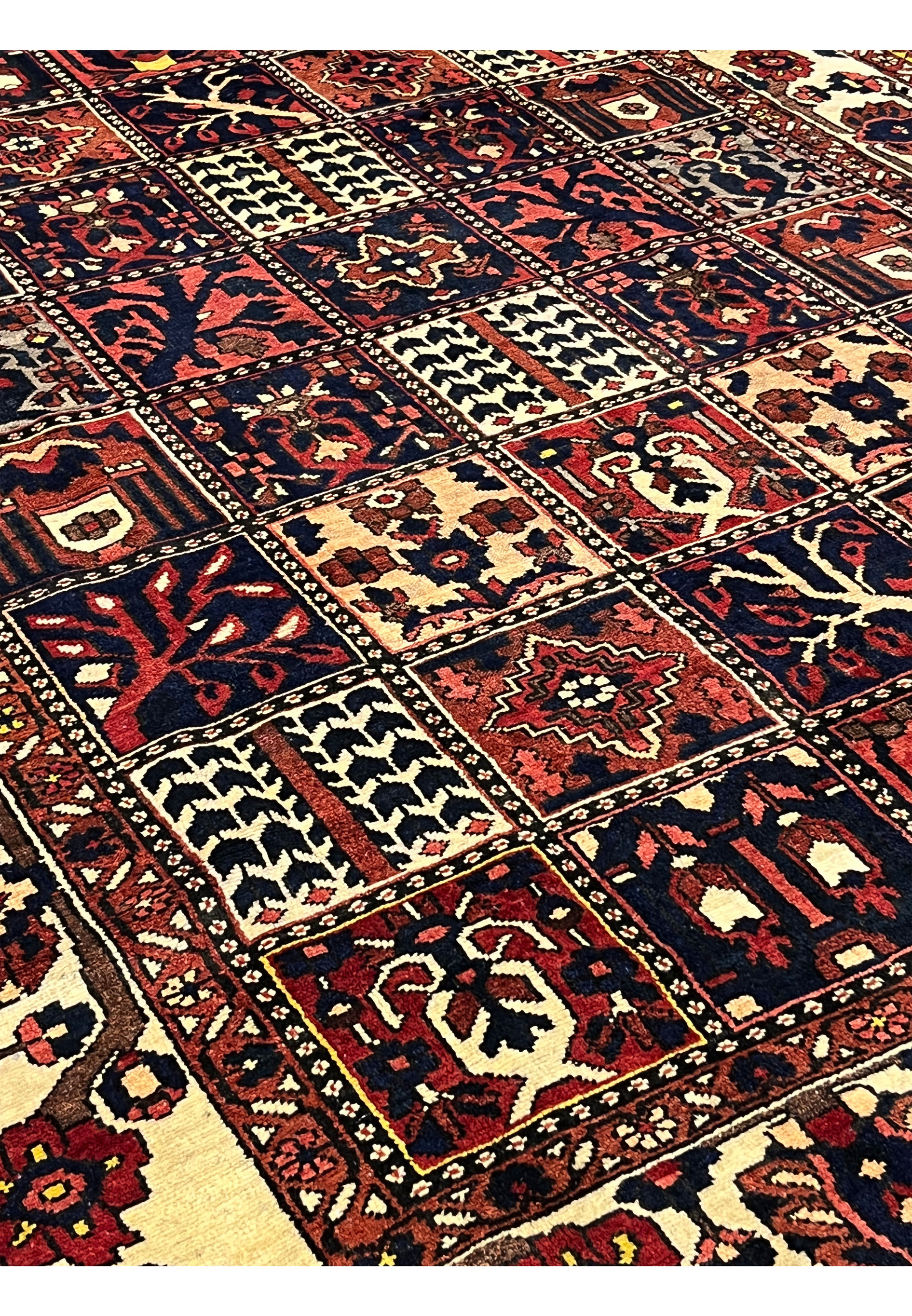 Side angle view of a Persian Bakhtiar garden rug showing depth, pile height, crisp panel layout, and the contrast between ivory borders and dark patterned field