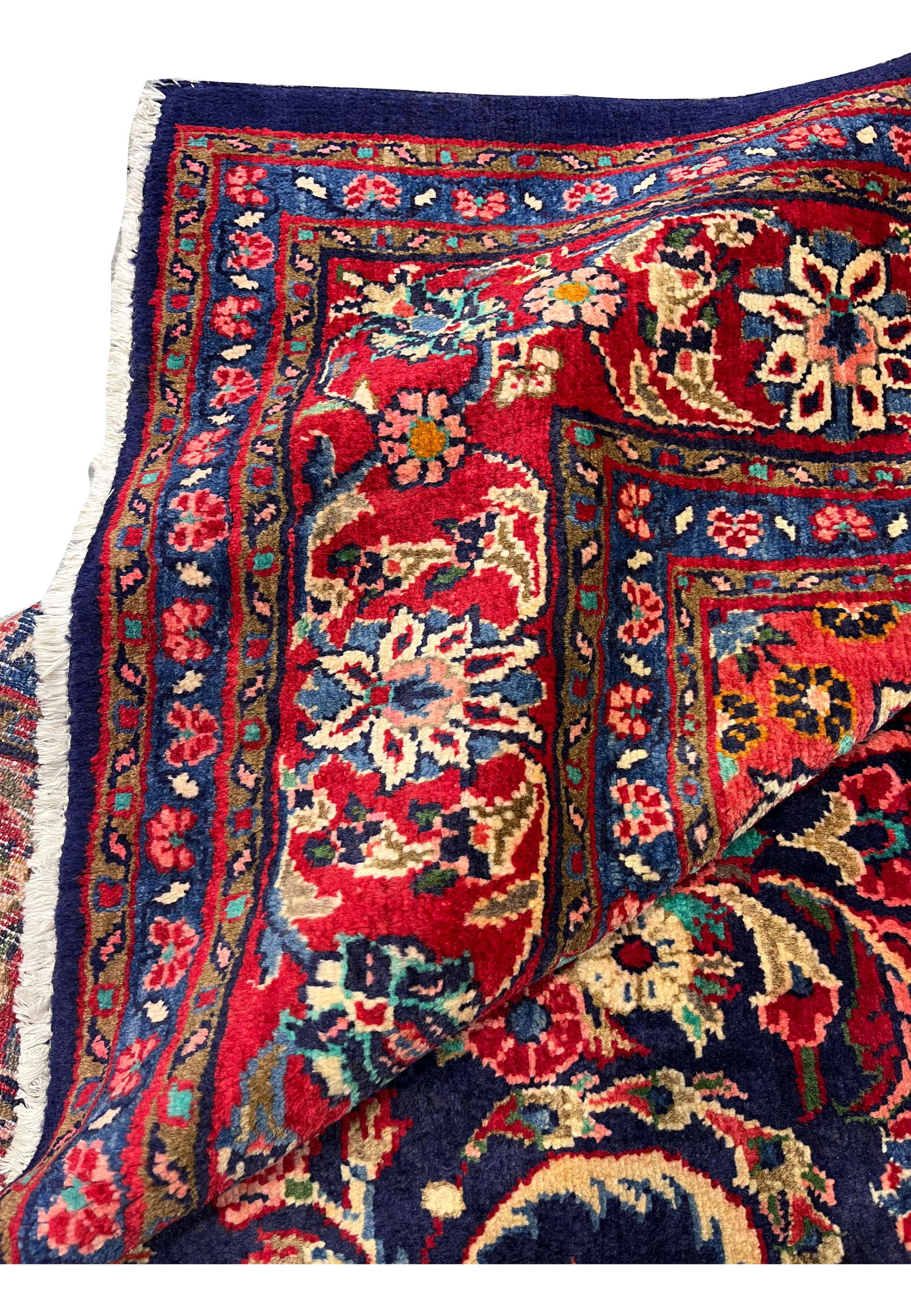 Folded corner showing rug thickness, soft wool texture, fringe edge, and detailed border motifs in red, navy, and ivory tones