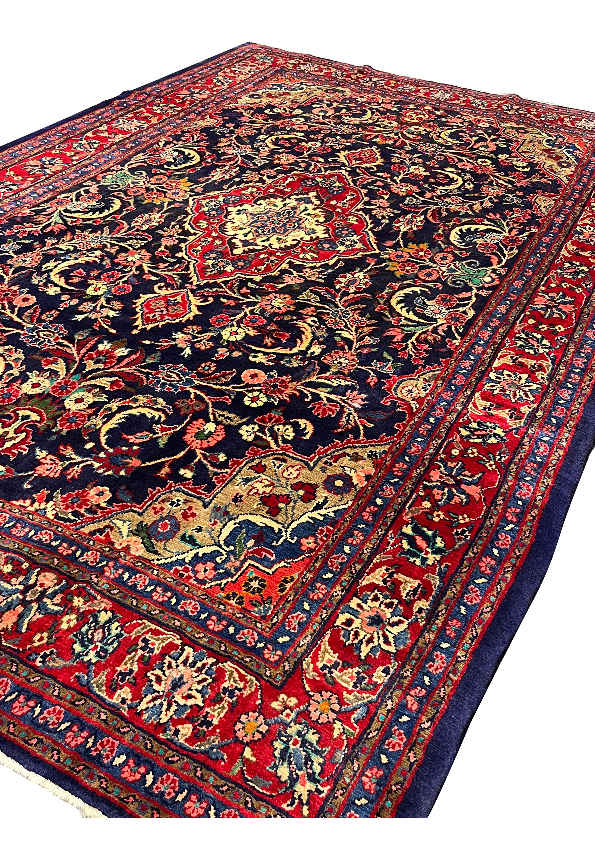 Persian Mahal rug shown from angled view with navy field, red borders, large floral vines, and central ivory medallion, thick wool pile texture visible