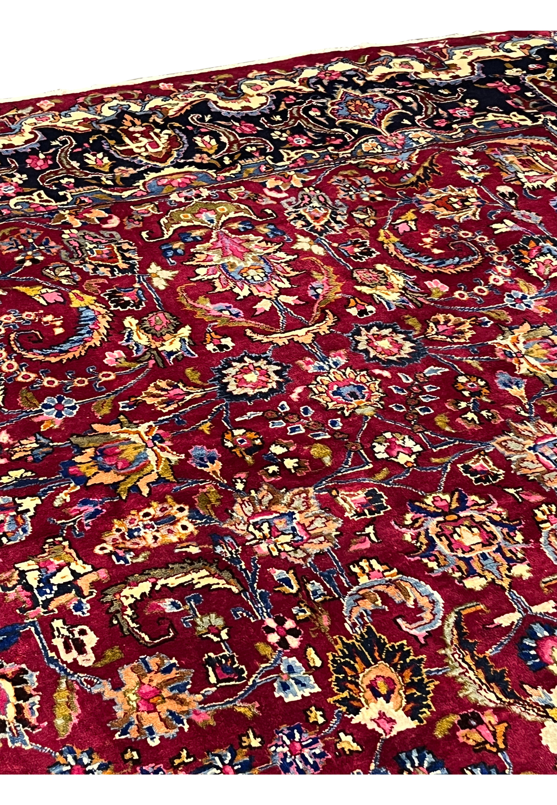 Design closeup of Persian Mashad rug showing symmetrical floral layout, brick red field, multicolor blossoms, and classic Persian composition.
