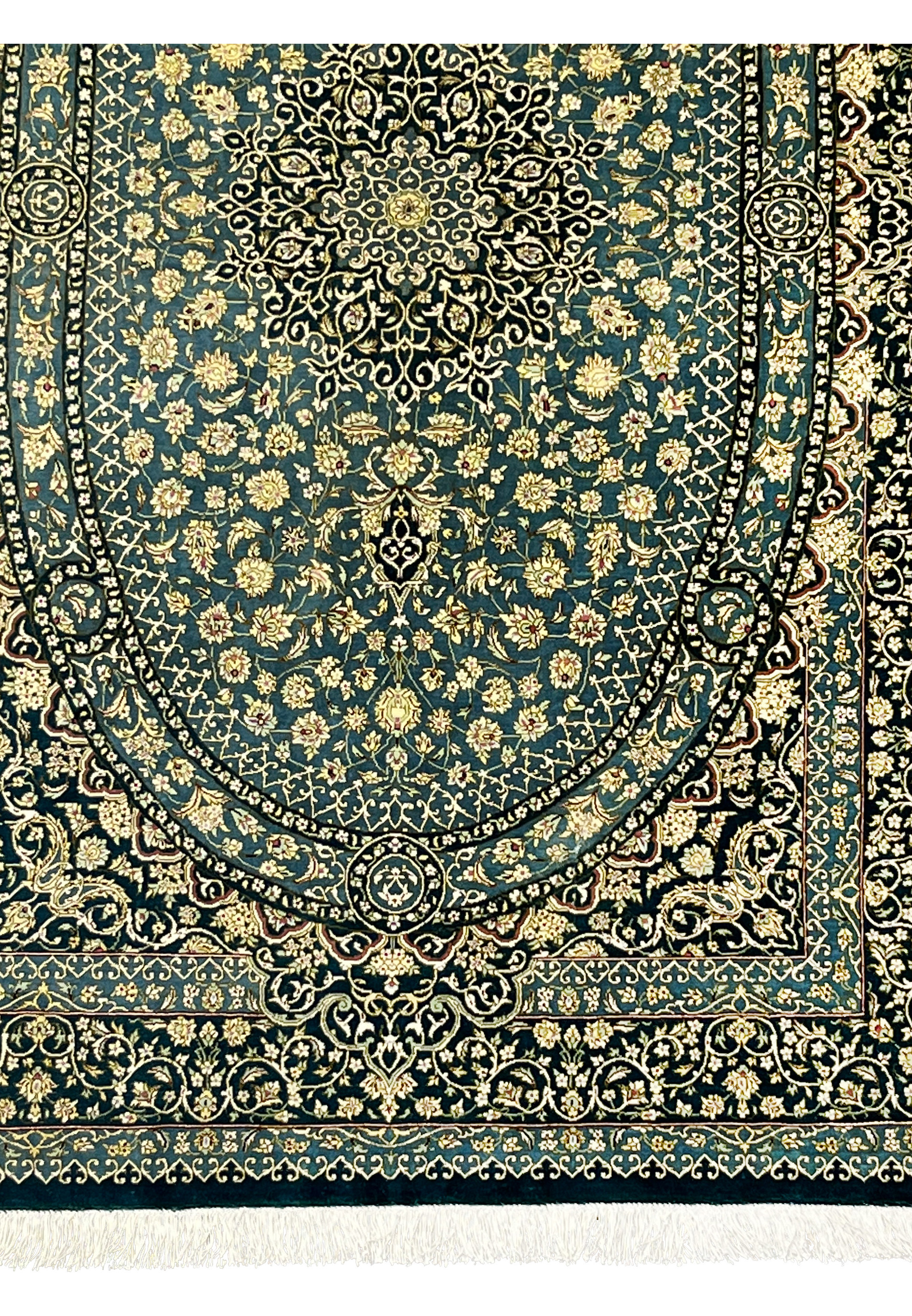 Lower section of silk Qum rug showing oval medallion base, dense florals and navy outlines with luminous teal silk background