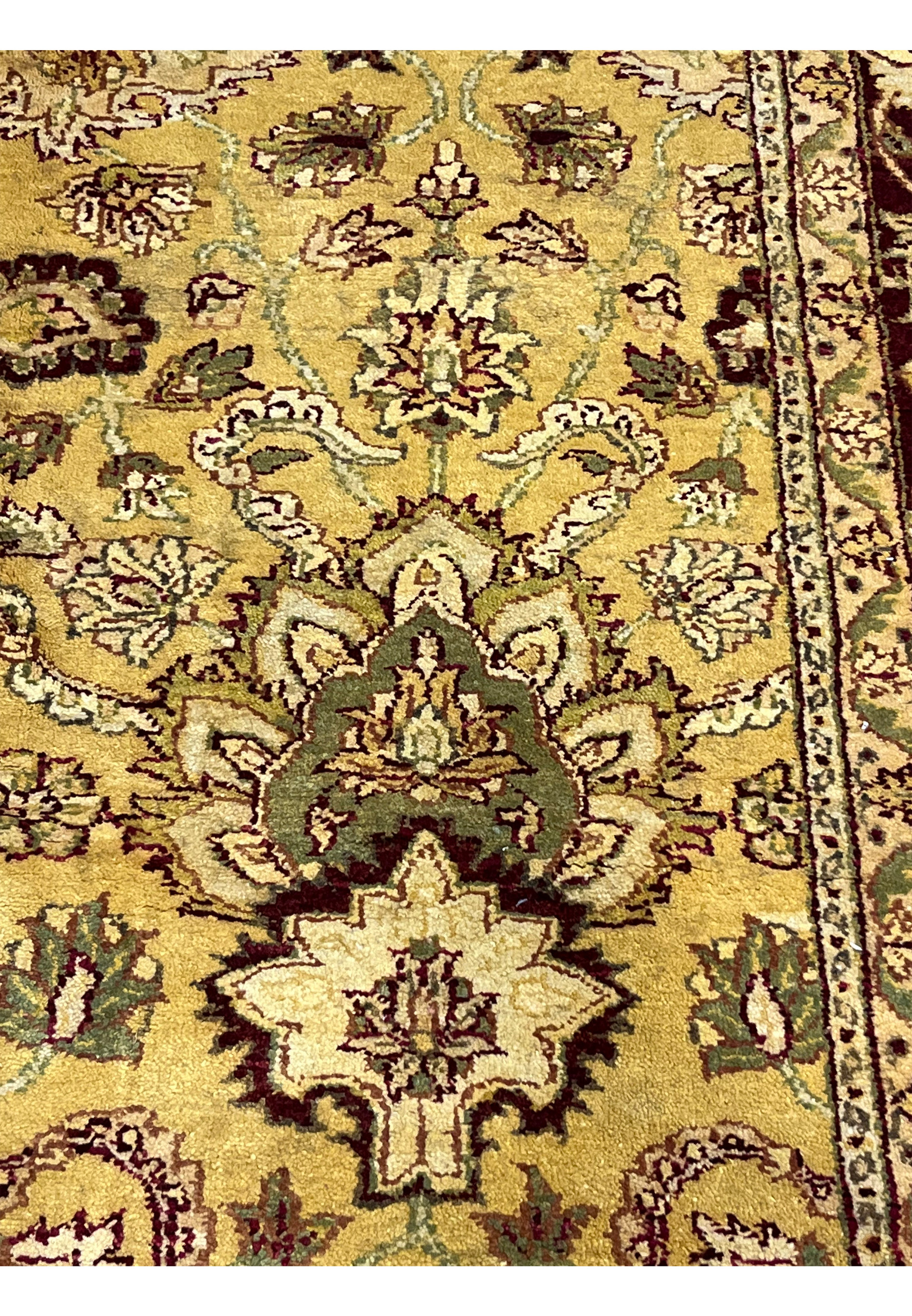 Detailed pattern section of 9x12 gold Agra rug featuring symmetrical floral elements and scrolling vines on warm mustard background.