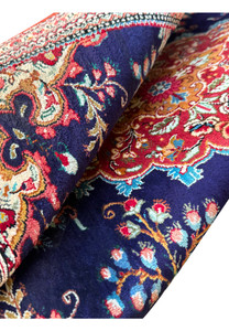 Folded Persian Qum silk rug showcasing the contrast of reds, blues, and creams in the complex designs