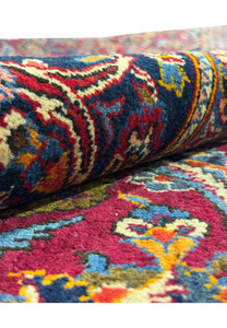 Partial roll-up view of a Persian Kashan rug revealing the pattern complexity with deep reds, blues, and accents of yellow and cream