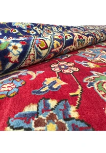 A 10 x 15'6" Persian Isfahan rug partially rolled, displaying the detailed patterns and vivid colors on the intricate border and the plush red field