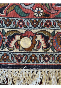 A close view of the Bijar rug's edge, featuring a coin for scale, showing the tight weave and elaborate border design