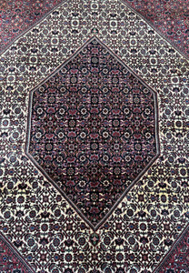 An overhead view of a Persian Bidjar rug, highlighting the central diamond medallion set against a detailed field of dark and light patterns